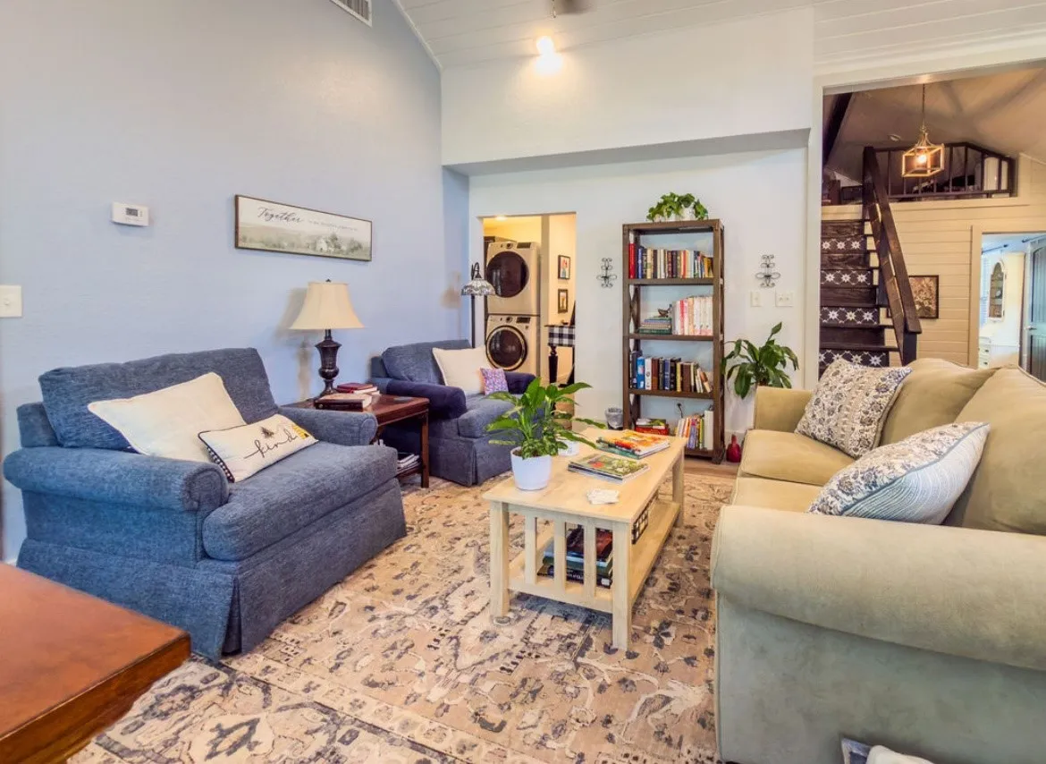 Living area featuring vaulted ceilings with wood paneling, wood-finish flooring, a built-in bookshelf, and a visible stacked washer and dryer unit