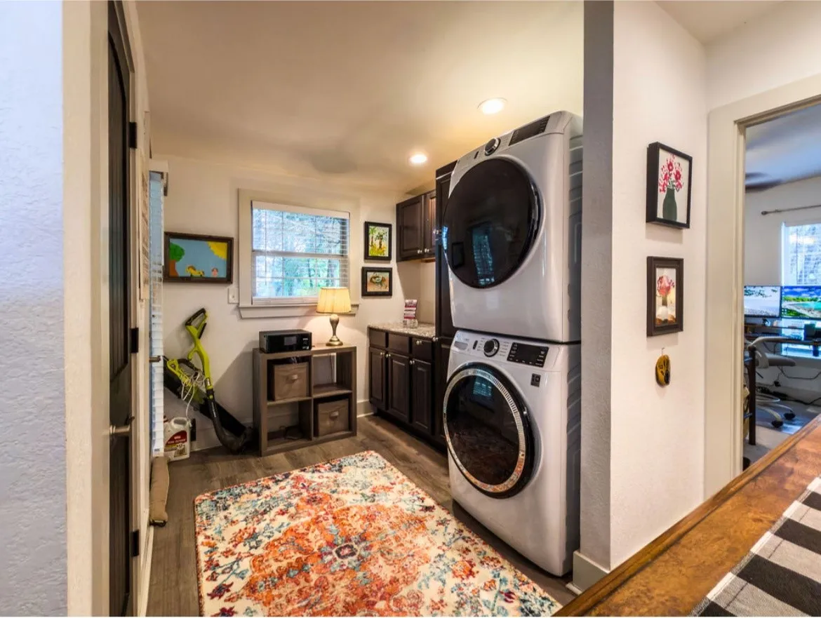 Dedicated laundry area featuring a stacked washer and dryer, wood-finish flooring, recessed lighting, built-in cabinetry, and a window with natural light