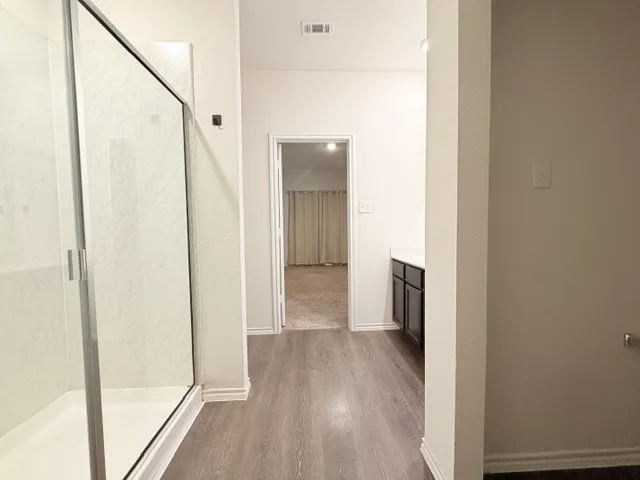 Spacious bathroom featuring a glass-enclosed shower, wood-finish flooring, and a dark wood-finish vanity with a light countertop