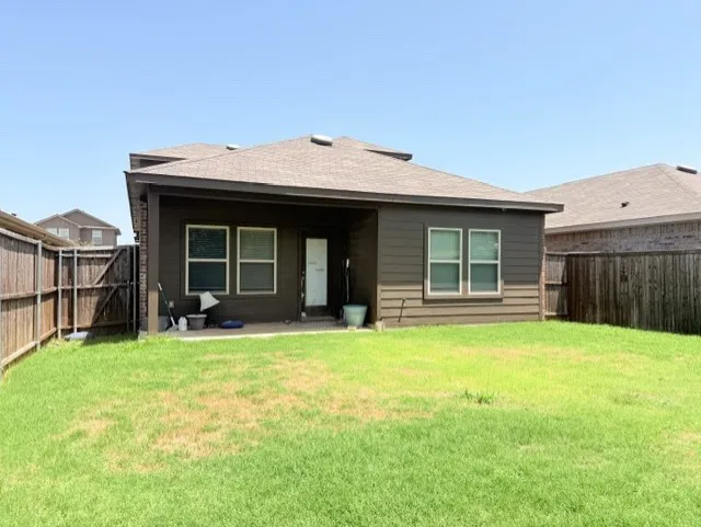 Expansive backyard featuring a green lawn, full privacy fencing, and a covered patio area