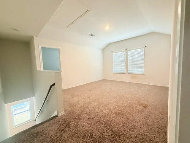 Spacious upper level room featuring vaulted ceilings, neutral carpeting, and two windows with horizontal blinds