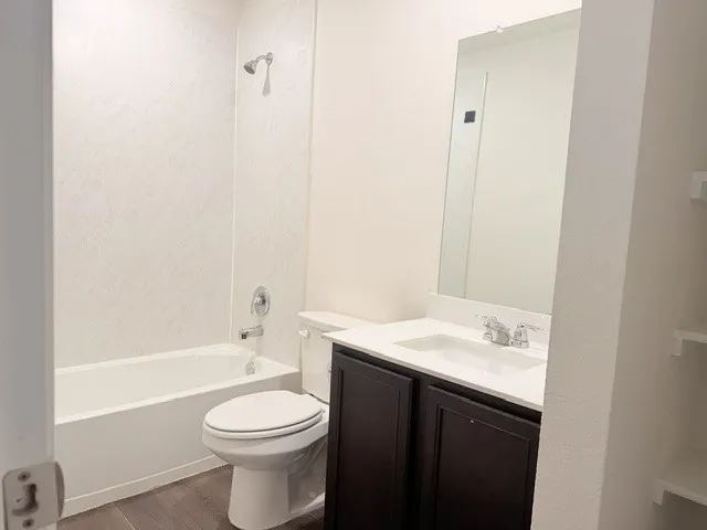 Bathroom featuring a full-size tub and shower combination with chrome fixtures, a dark wood-finish vanity with a white countertop and integrated sink, a frameless mirror, and wood-finish flooring