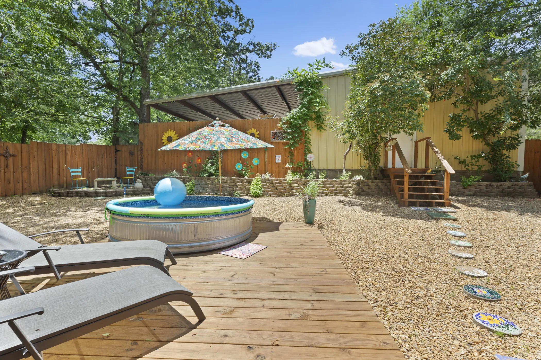 Backyard area featuring a wood-plank deck, gravel landscaping, and a metal stock tank