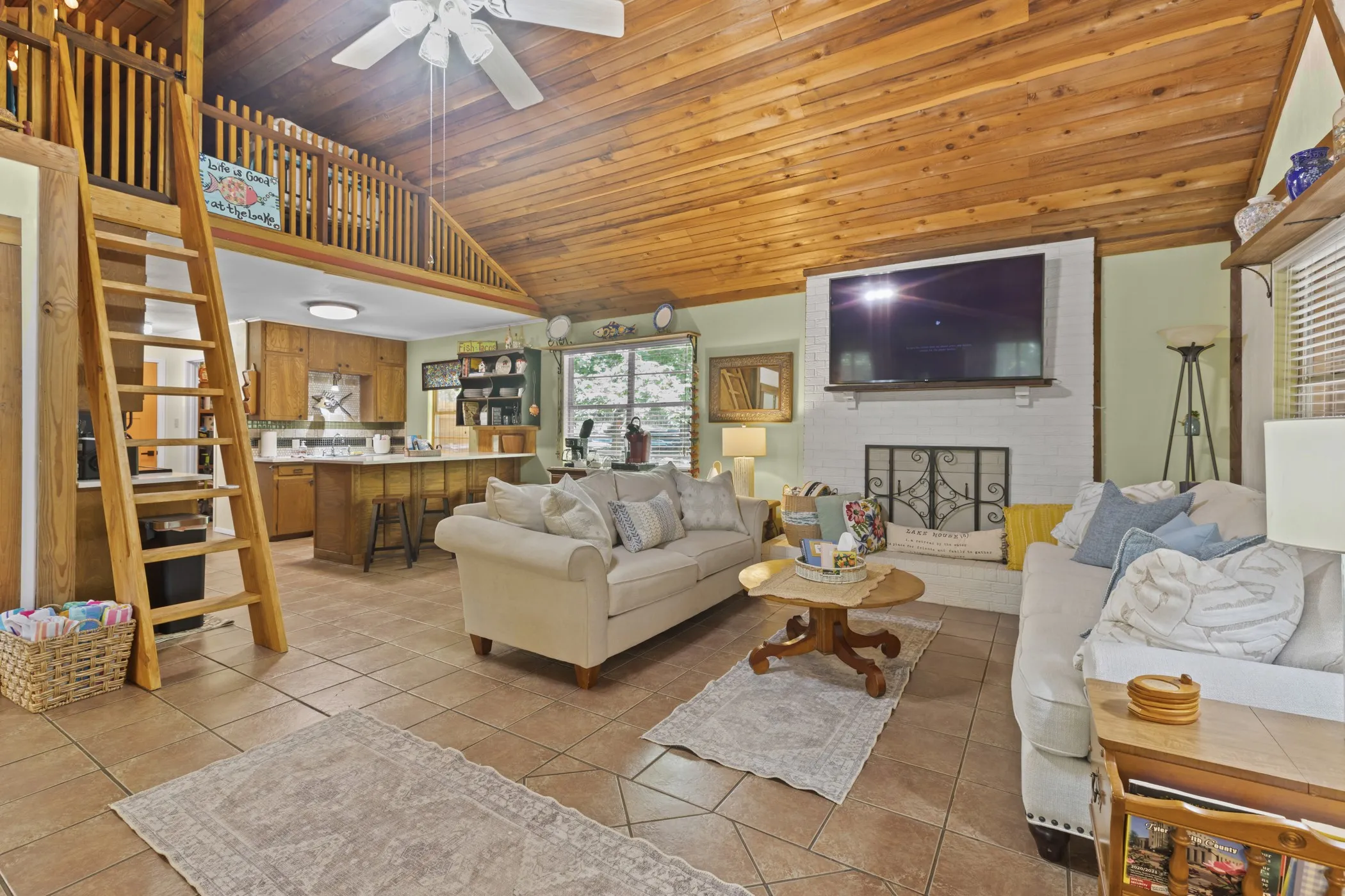 Open-concept living area featuring a vaulted wood-finish ceiling, tile flooring, and a white brick fireplace with a decorative screen
