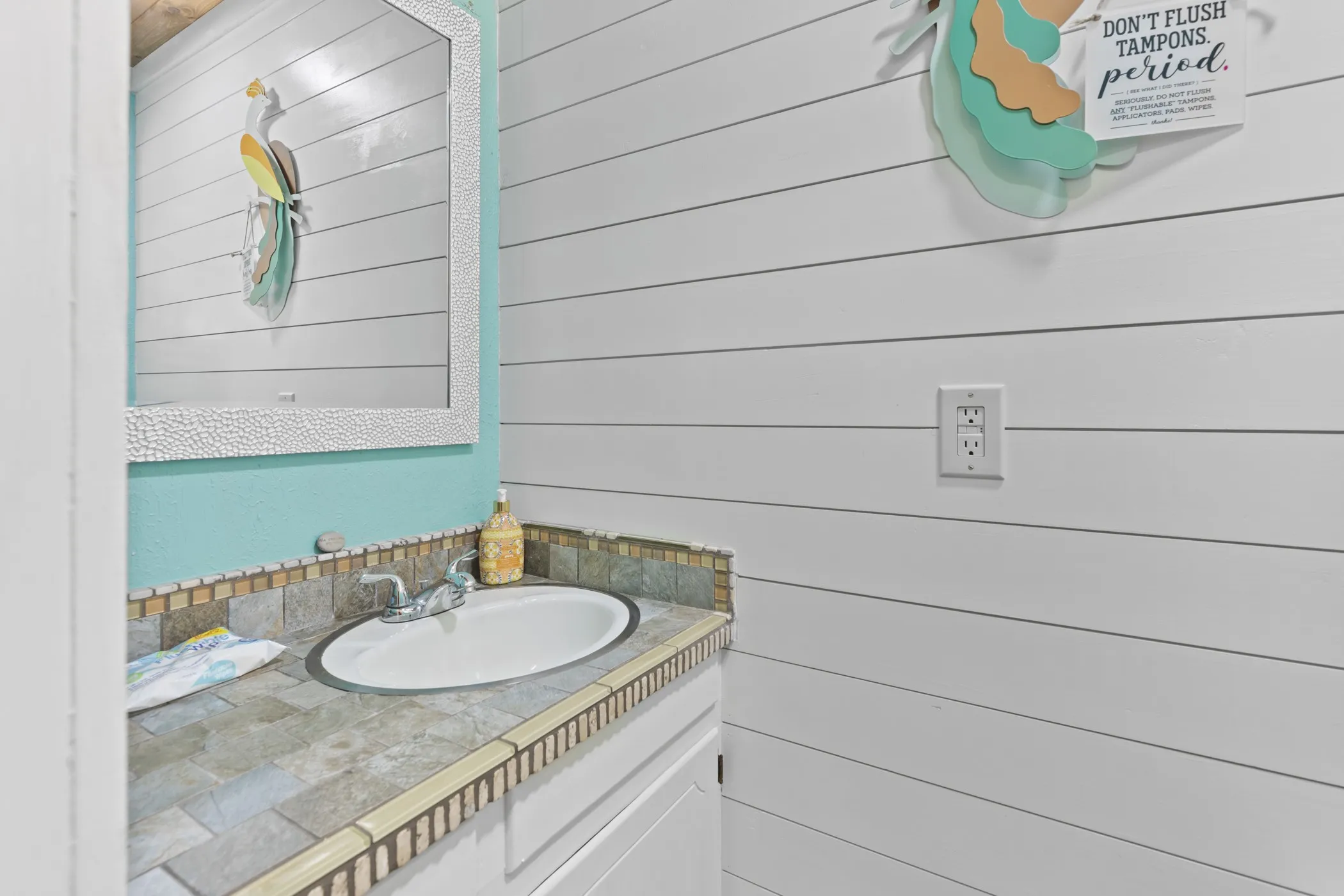 Vanity featuring a tiled countertop and integrated sink, complemented by a textured framed mirror