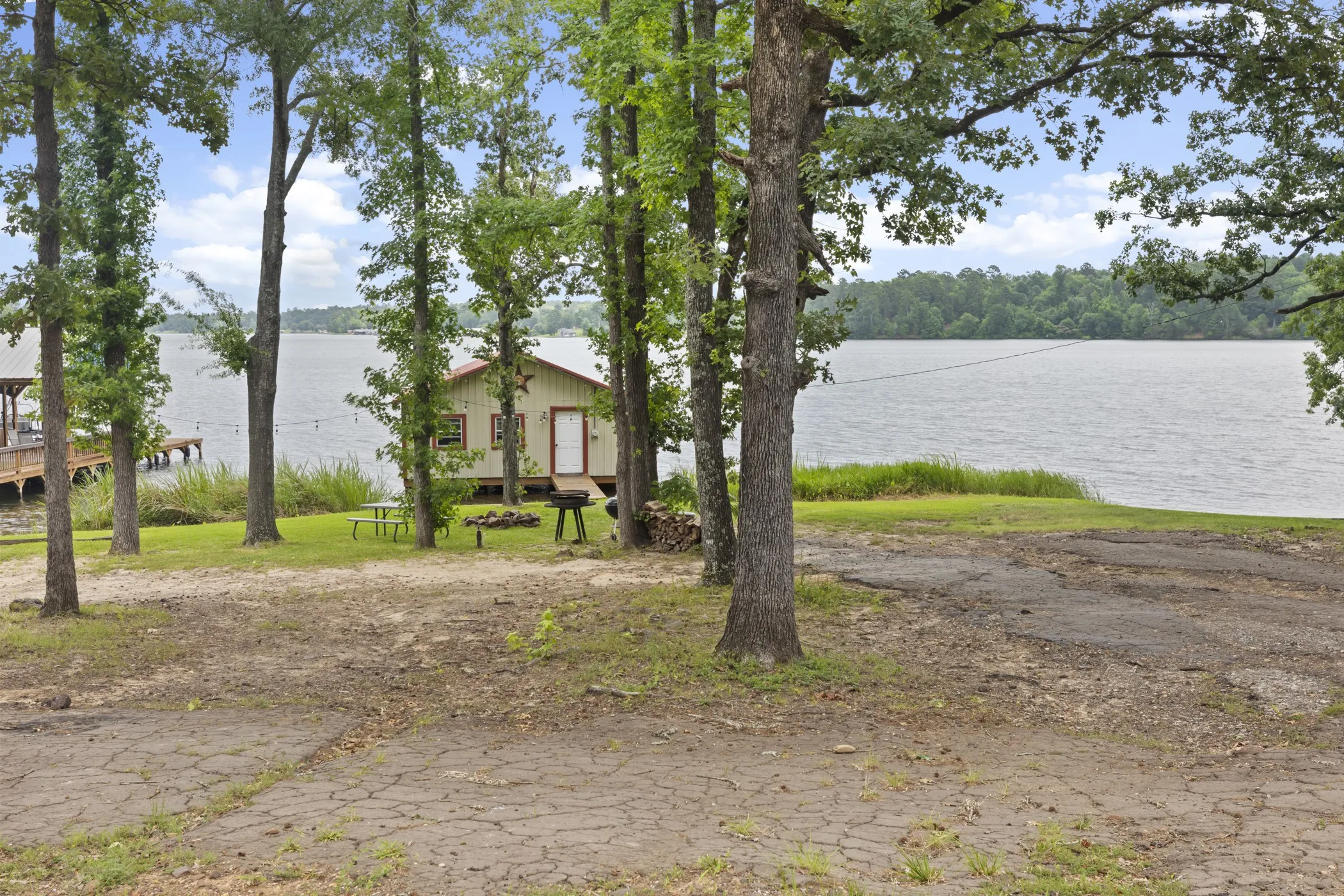 Waterfront property with a single-story structure, a boat dock extending into the water, mature trees, and a spacious outdoor area