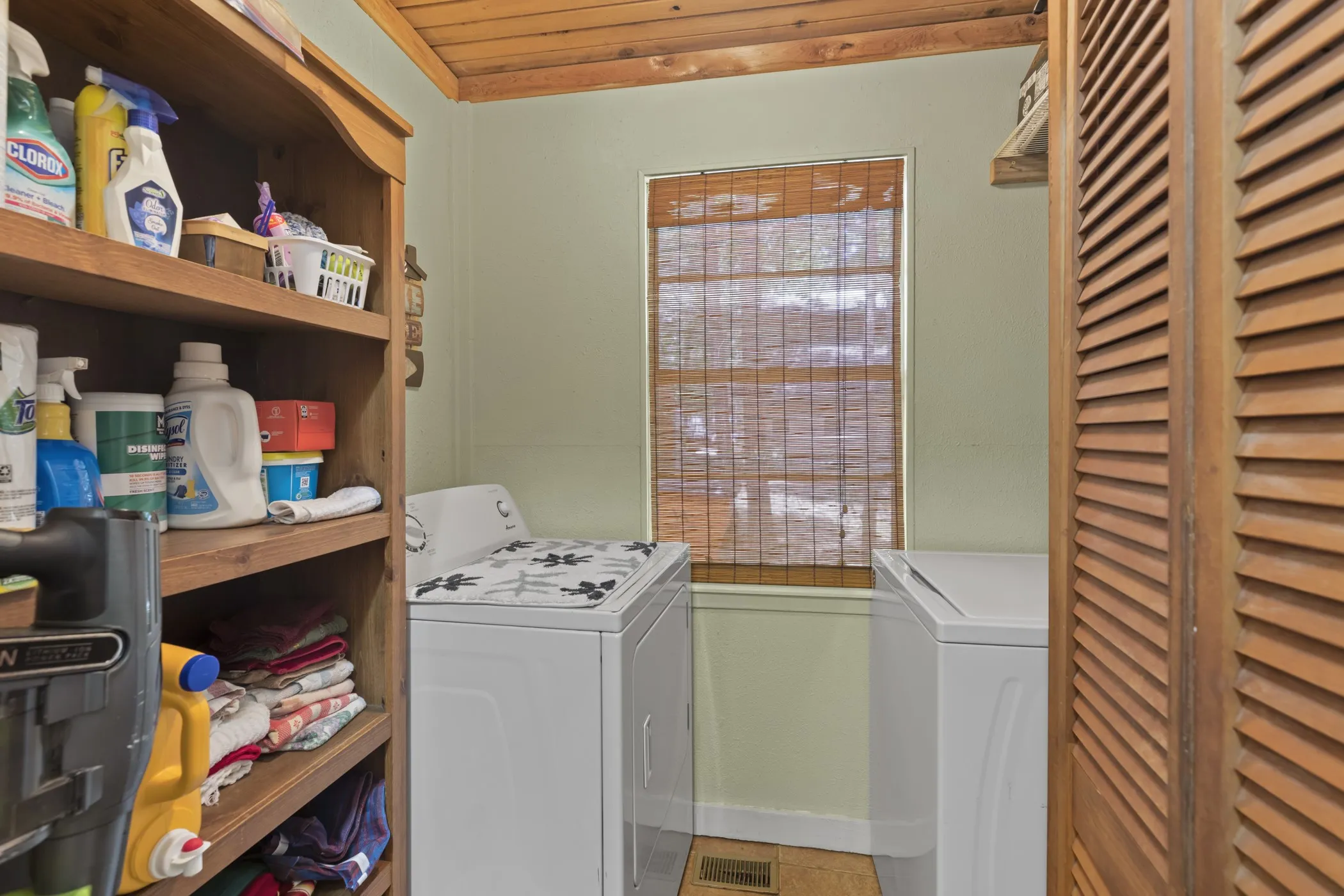 Dedicated laundry area featuring a wood-finish ceiling, built-in shelving, louvered bi-fold doors, and a window with a natural fiber blind