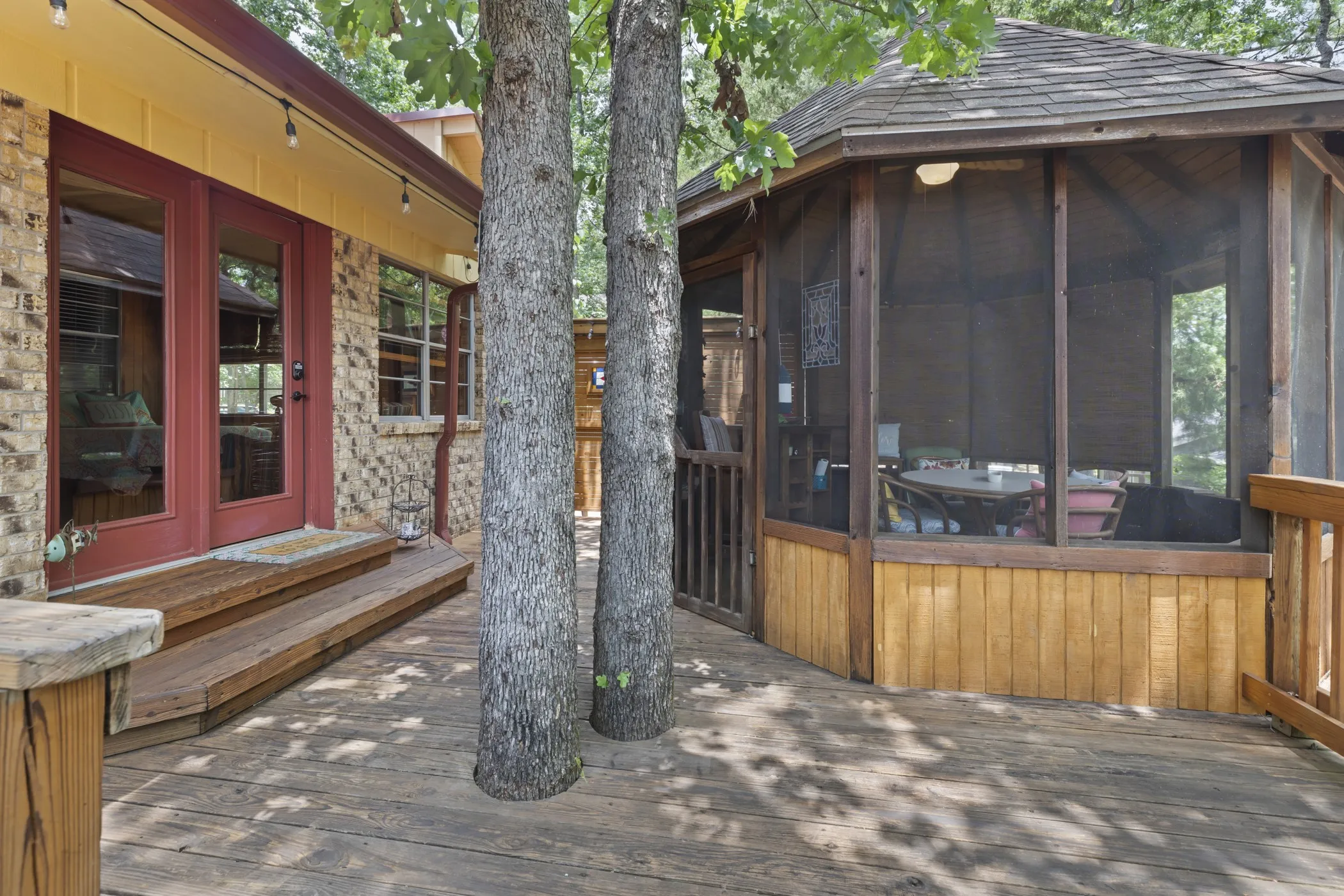 Expansive wood-finish deck featuring an octagonal screened-in gazebo with a cedar shake roof and a brick exterior with red double doors and exterior string lighting