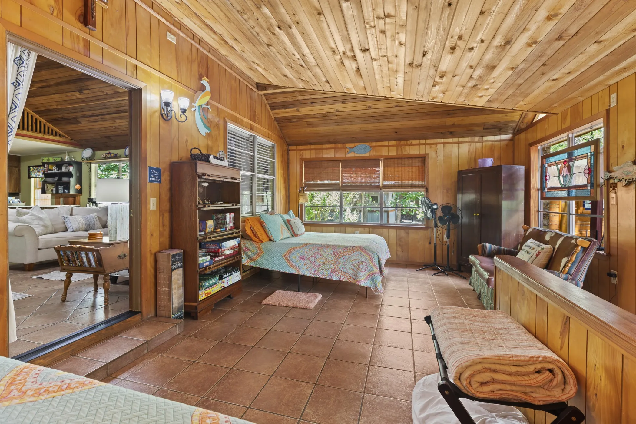 Room featuring wood-paneled walls and ceiling, tile flooring, multiple windows, and an opening to an adjacent interior space
