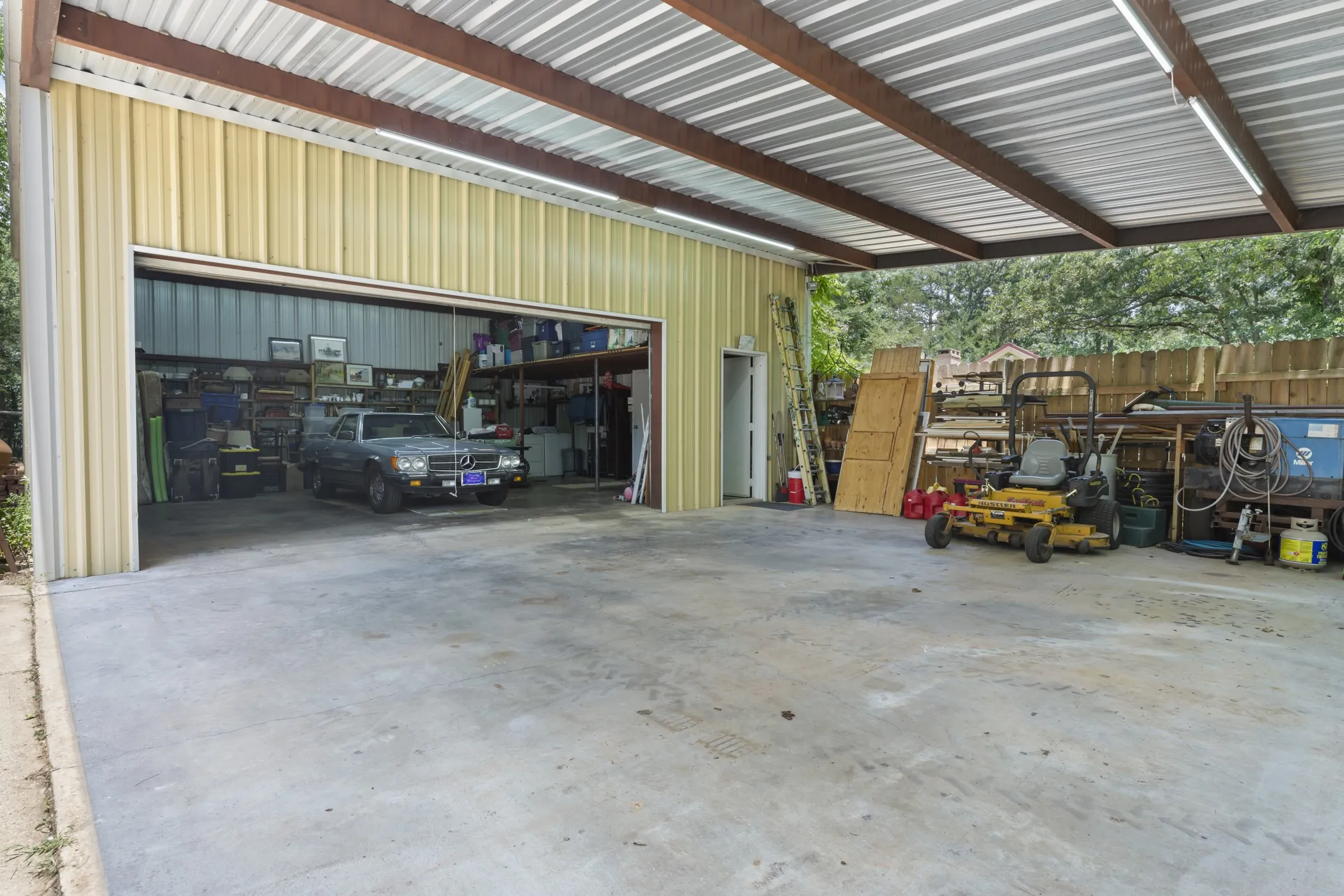 Expansive covered concrete pad with corrugated metal roofing, exposed wood beams, and fluorescent strip lighting