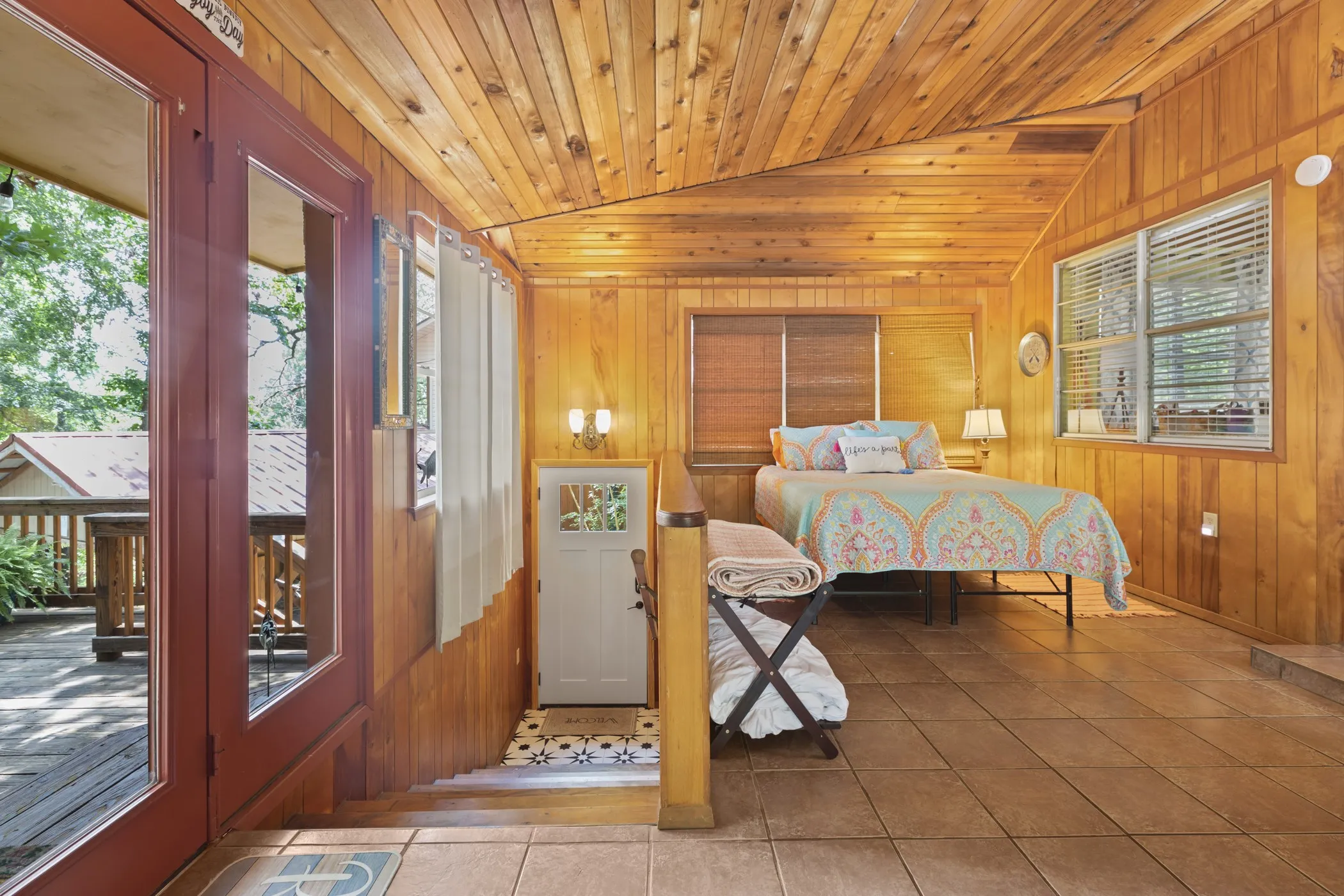 Interior space featuring extensive wood paneling on walls and ceiling, a red-framed glass-paneled door opening to an exterior deck, and a tiled flooring