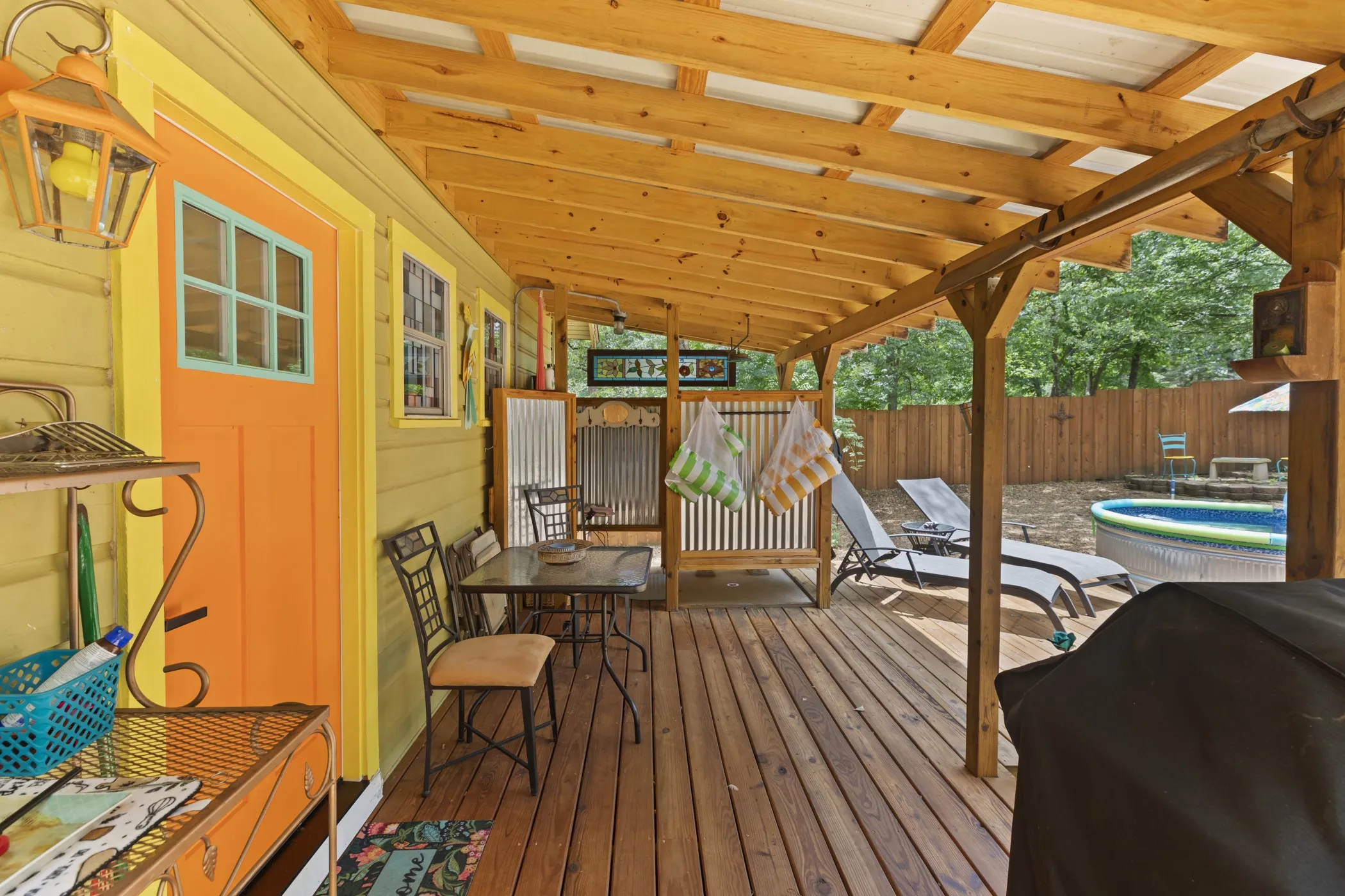 Covered wood-plank deck featuring a dining area, corrugated metal privacy screens, and a wood privacy fence