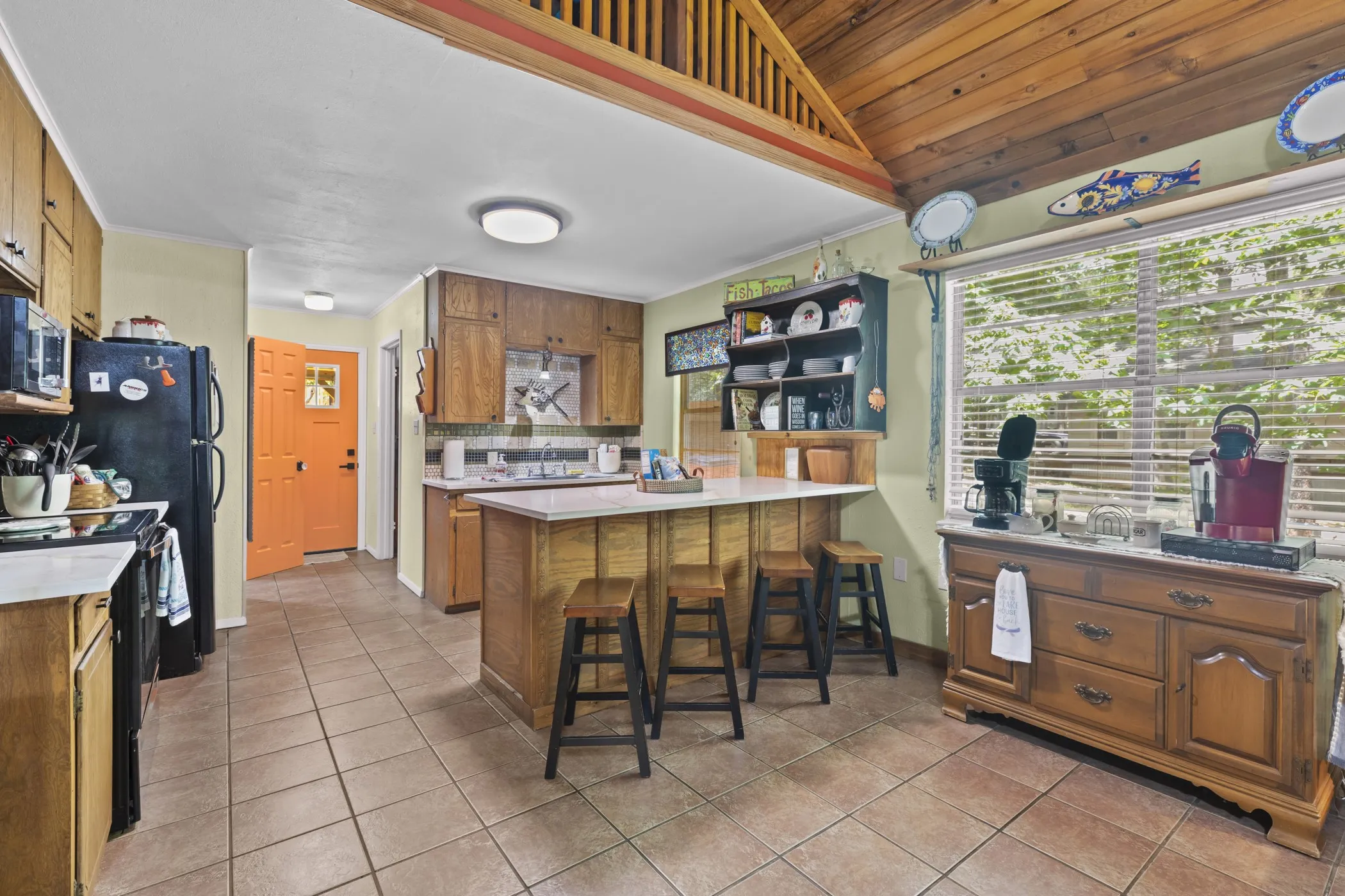 Kitchen featuring tile flooring, wood cabinetry, an island with countertop seating, a window with horizontal blinds, and a wood plank vaulted ceiling