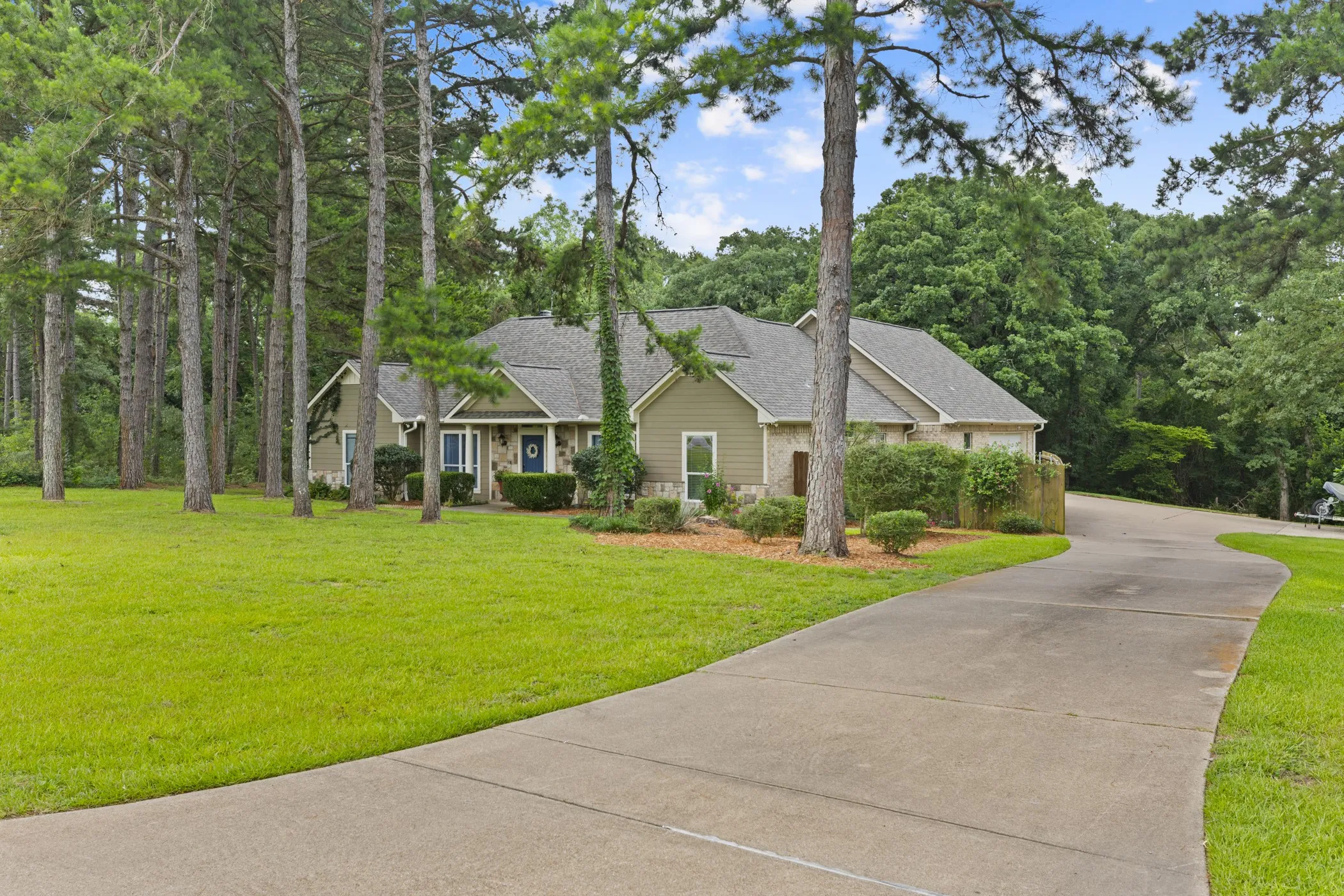 Stone and siding exterior with a dark shingle roof, surrounded by mature trees