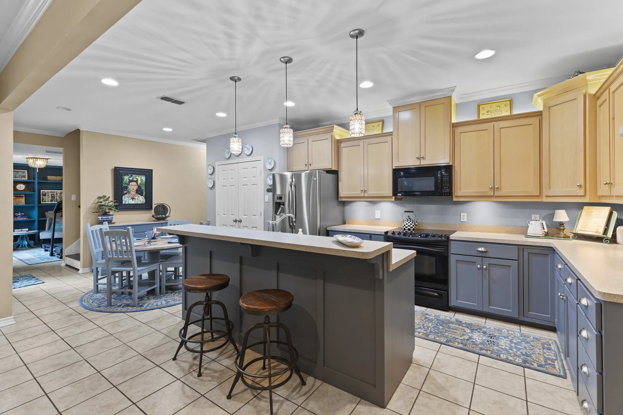 Kitchen featuring a breakfast bar with paneling, two-tone cabinetry, stainless steel refrigerator, black range, and recessed lighting