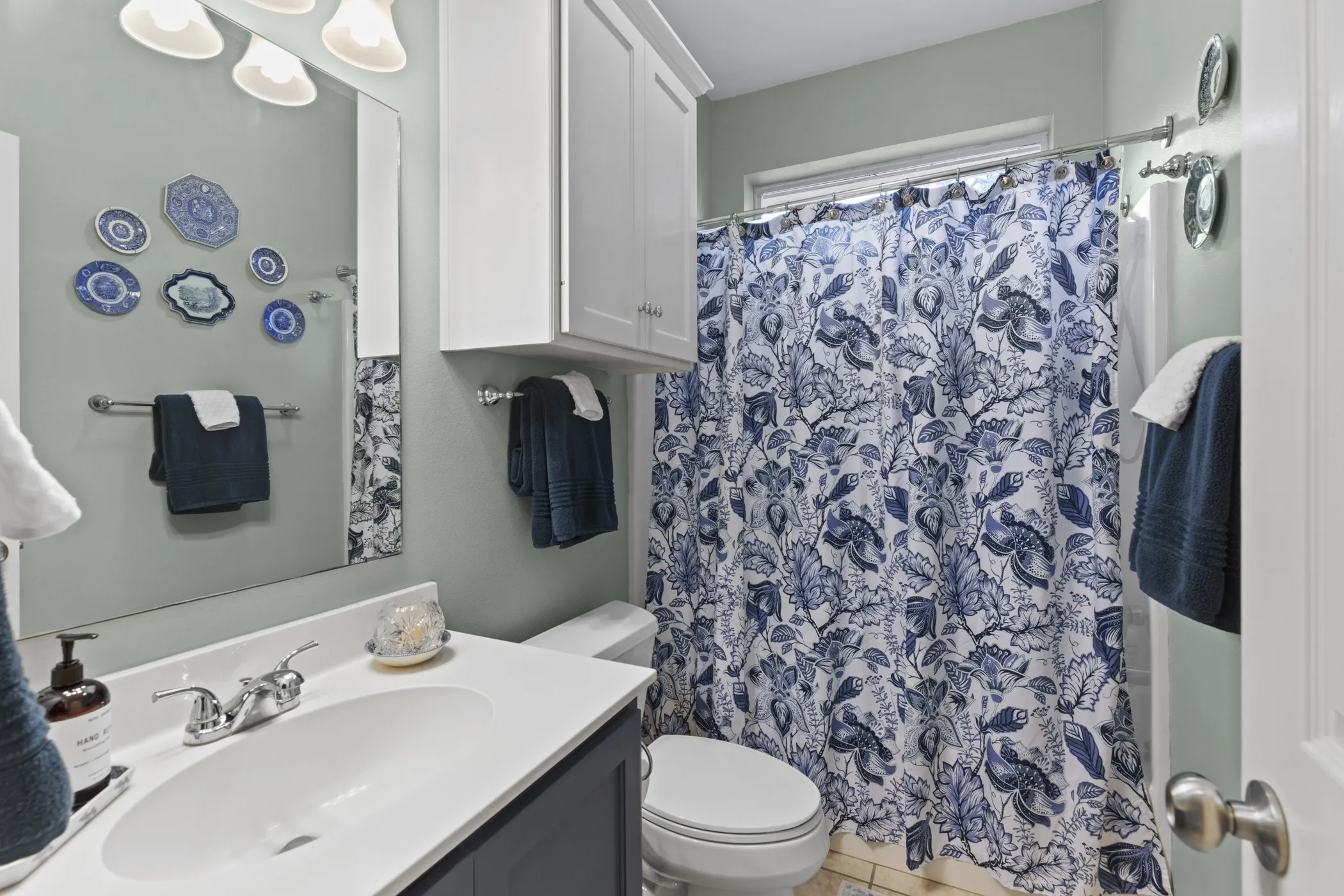 Bathroom featuring a single vanity with an undermount sink, chrome faucet, white countertop, and dark blue base cabinetry