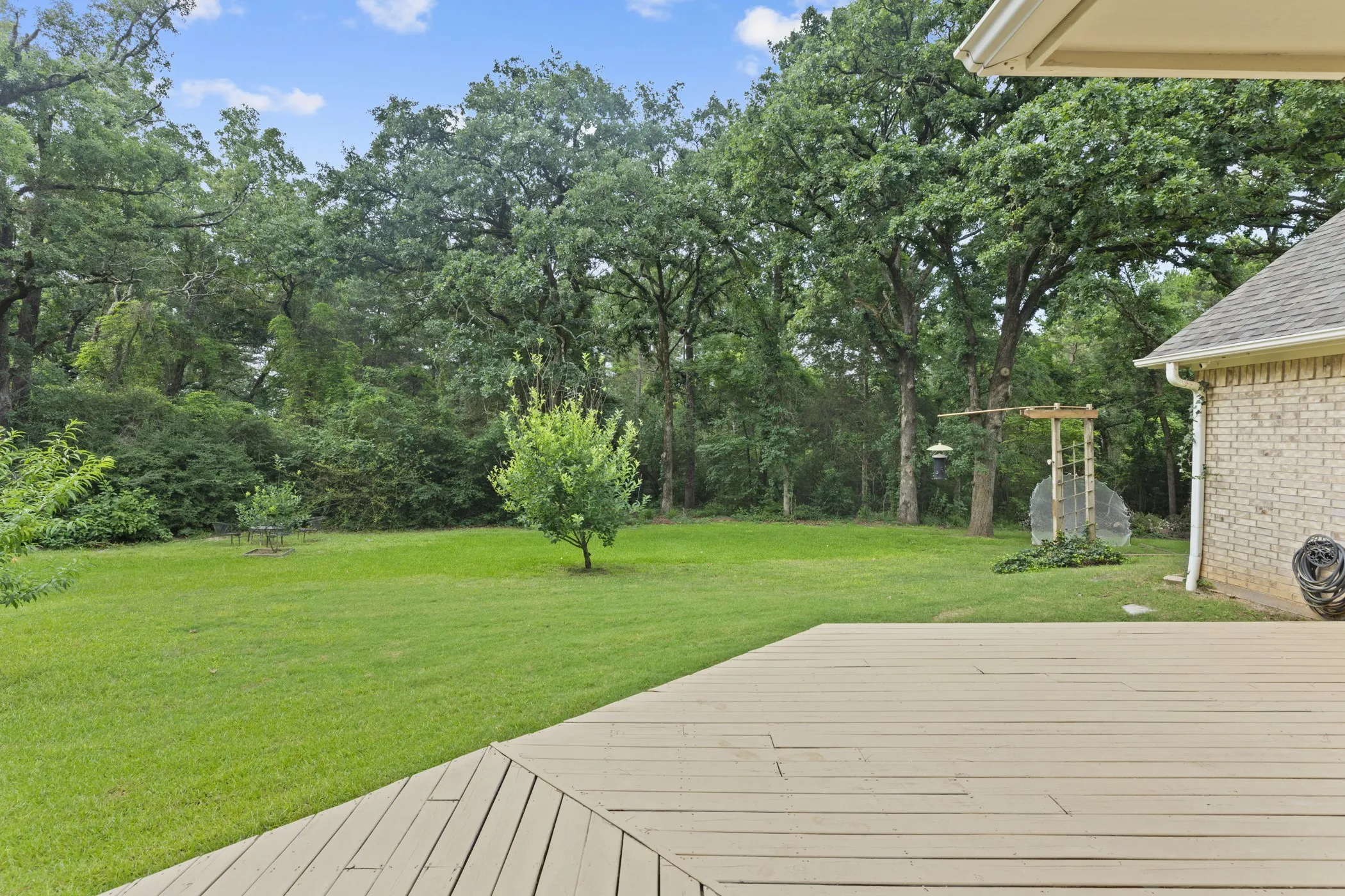 Expansive green lawn with mature trees, a private wooden deck, and a brick exterior