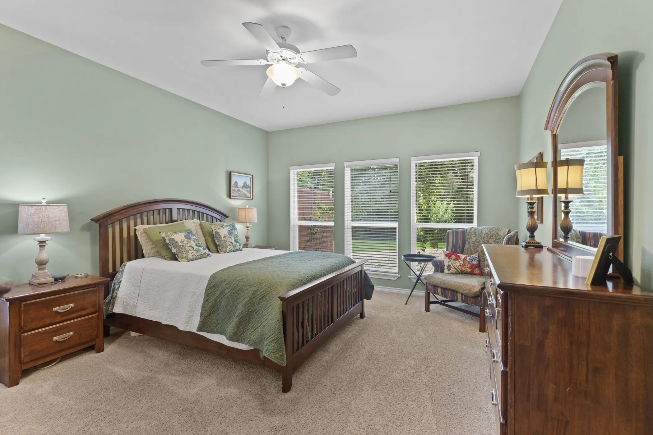 Spacious bedroom featuring neutral carpeting, a ceiling fan with integrated lighting, and multiple windows with blinds