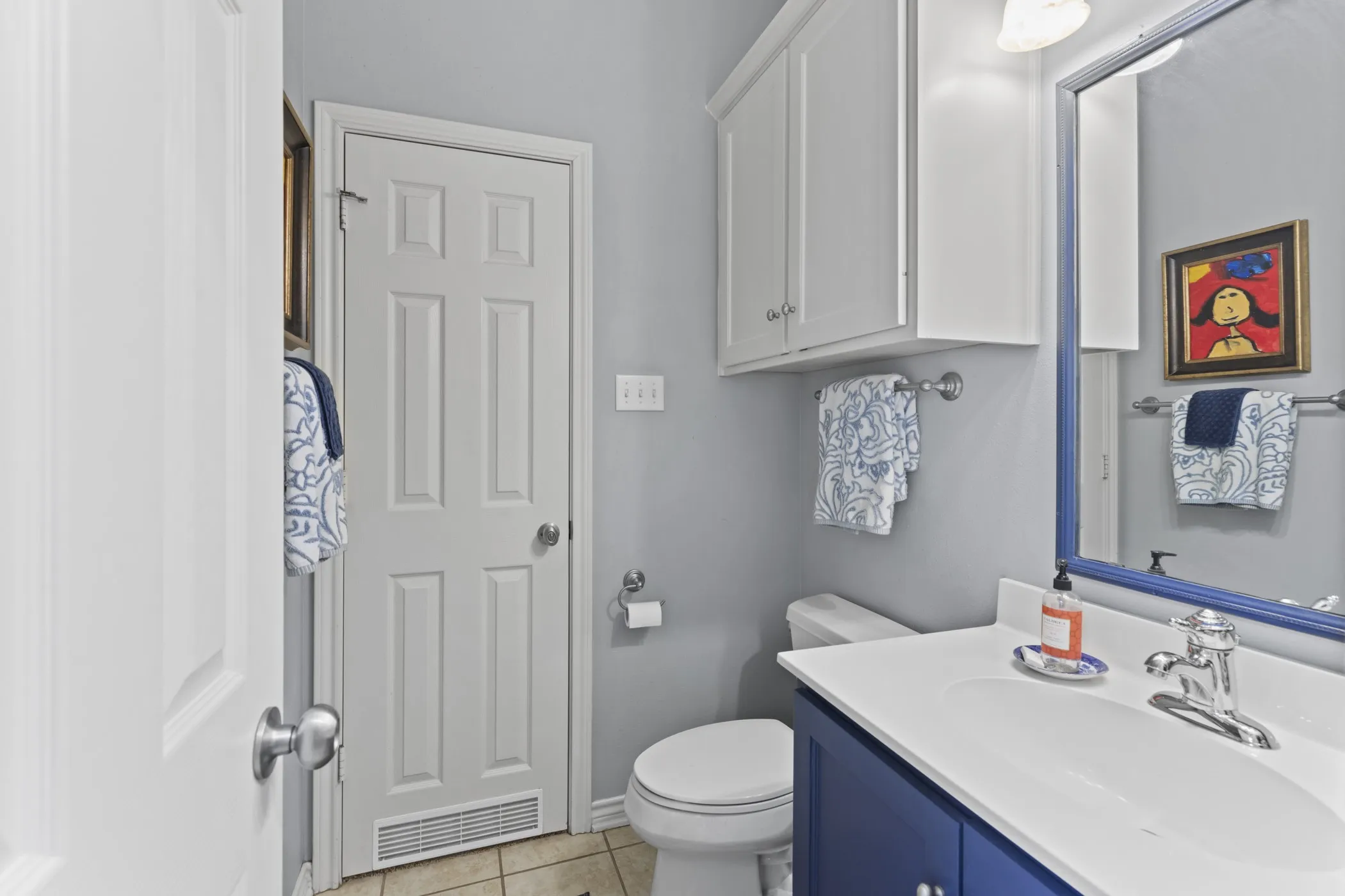 Bathroom featuring a blue vanity with a white countertop and integrated sink, a large wall-mounted mirror, white paneled doors, and overhead white cabinetry