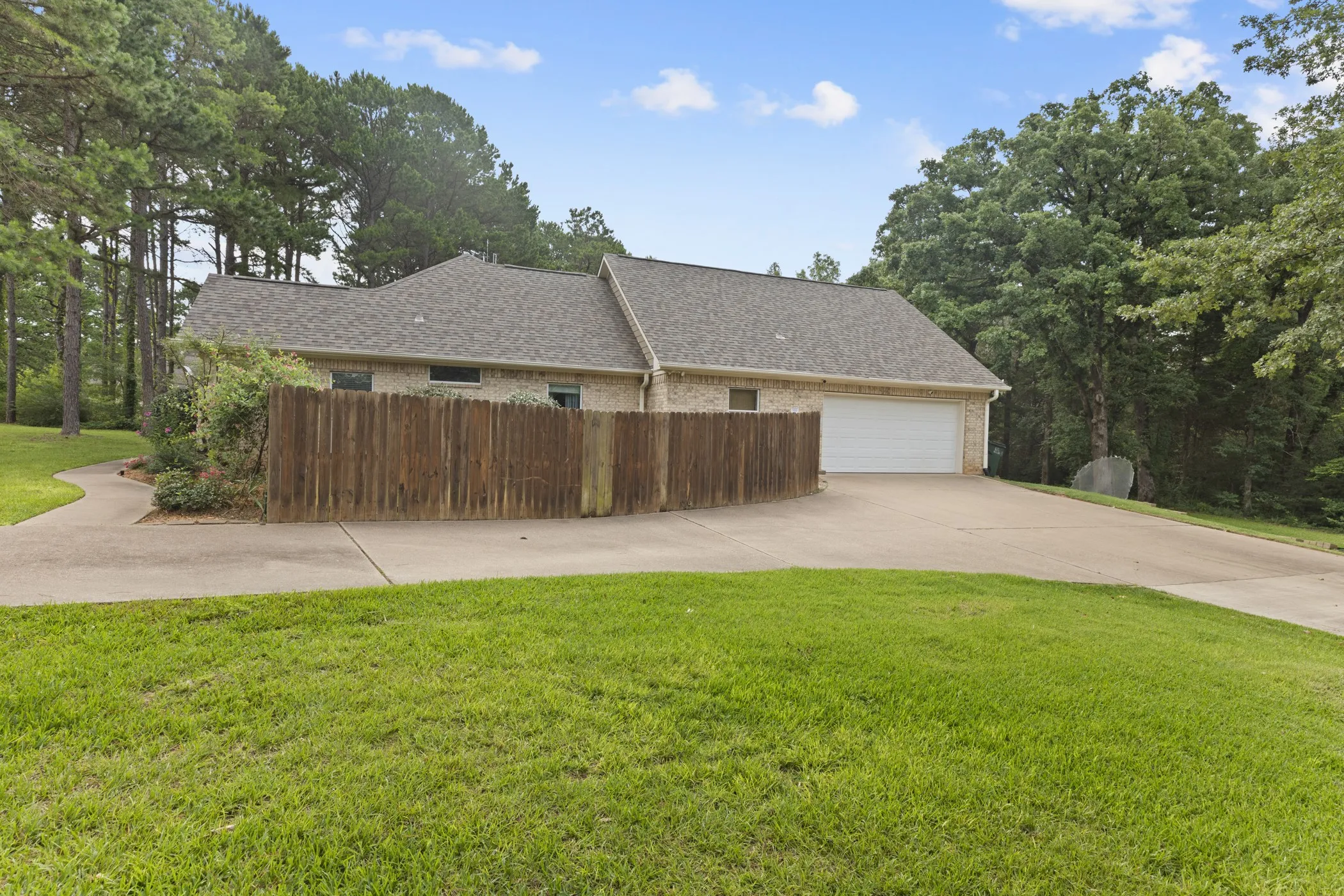 Brick exterior residence featuring a two-car garage, concrete driveway, and a wood privacy fence