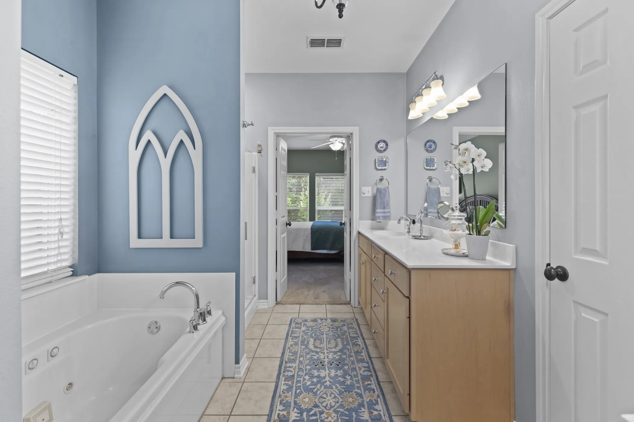 Bathroom featuring a large jetted tub, dual vanity with light-colored countertop, and tiled flooring