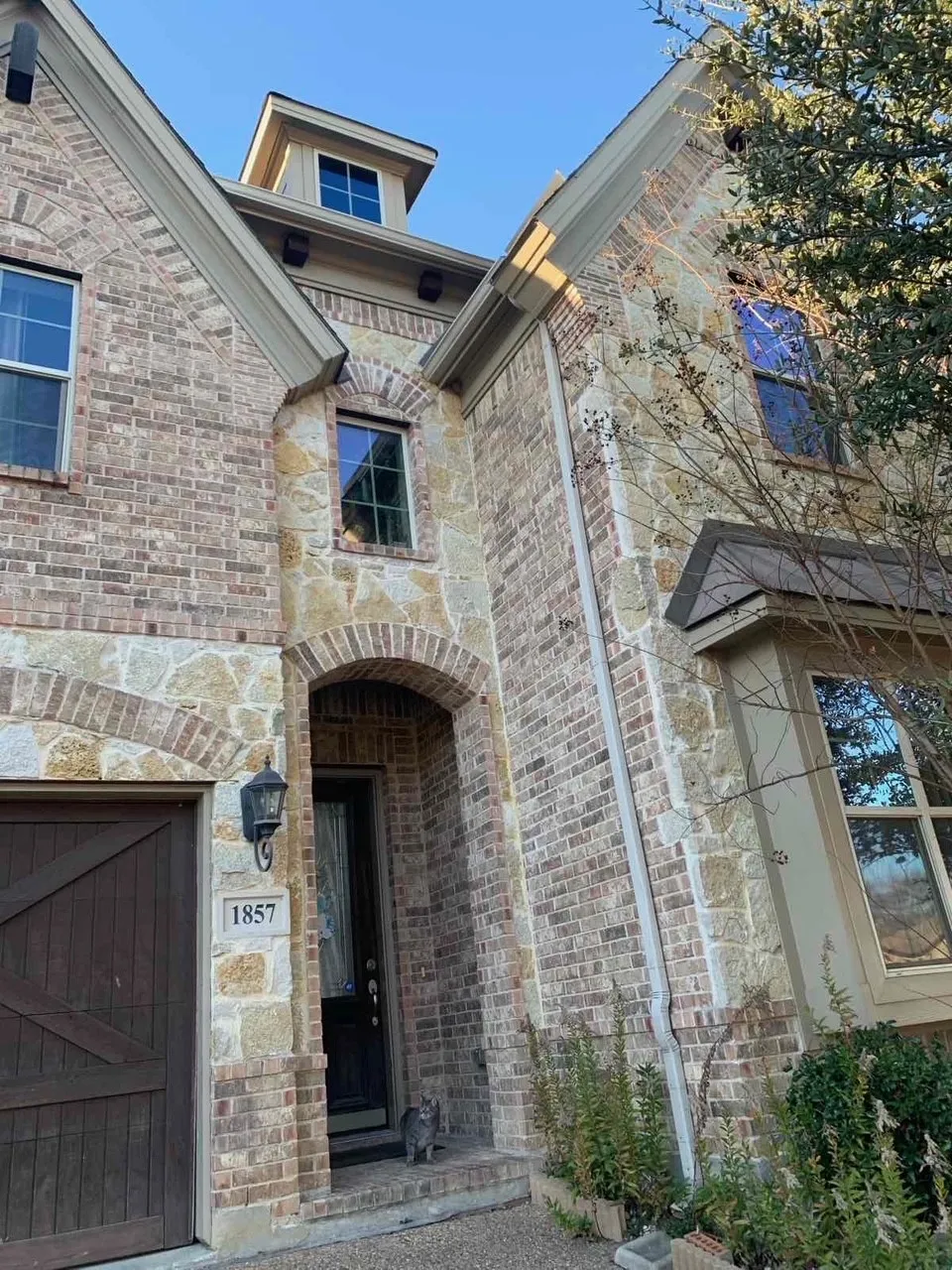Brick and stone facade featuring an arched entryway, decorative garage door, and bay window