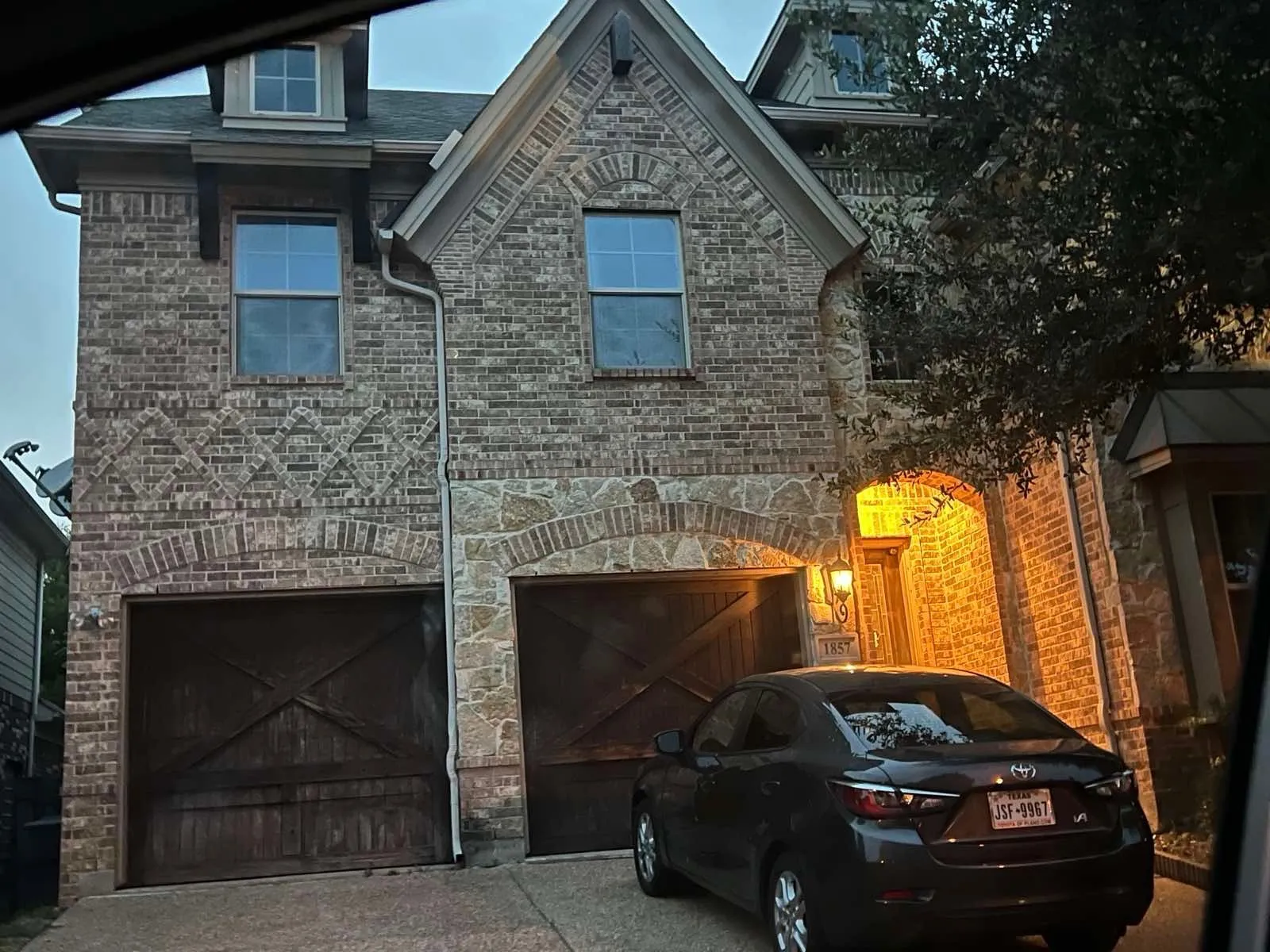 Brick and stone facade featuring arched garage entrances, multi-pane windows, and prominent dormer windows