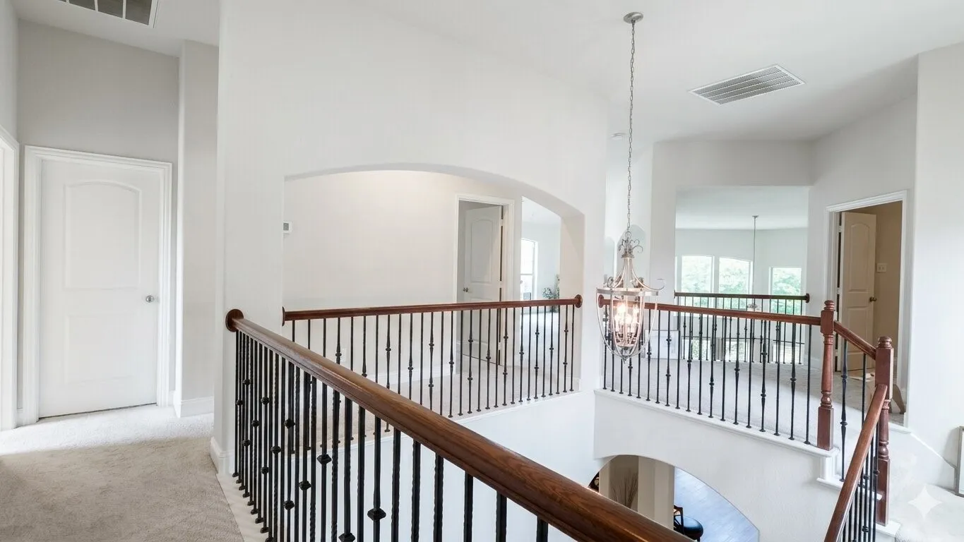 Upper-level landing featuring a chandelier, arched doorways, light carpeting, and dark wood handrails with wrought iron balusters