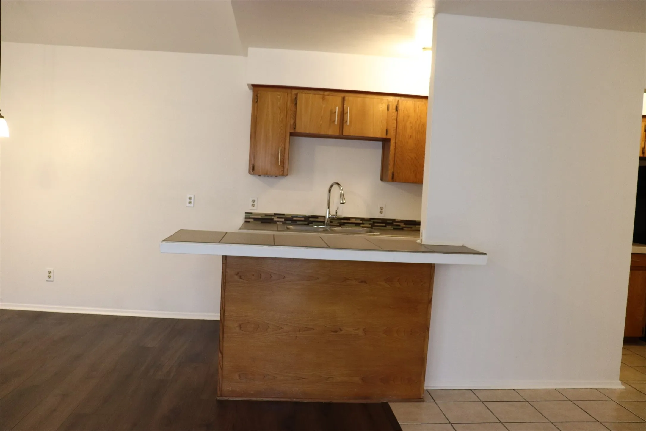 Kitchen featuring a breakfast bar with tile countertop, wood-finish cabinetry, stainless steel faucet, and tile backsplash