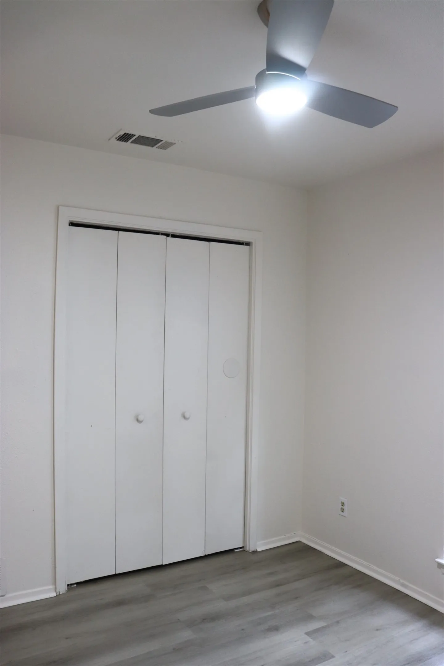 Room featuring wood-finish flooring, white walls, and a modern ceiling fan with integrated lighting