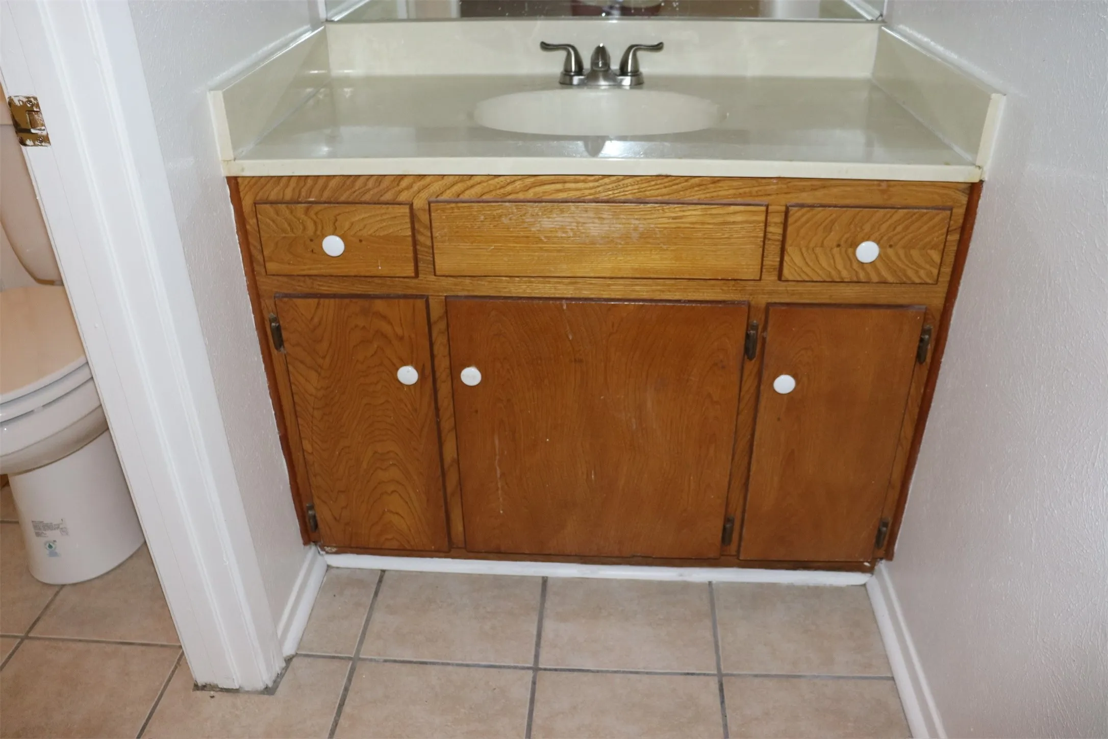 Bathroom vanity featuring a wood-finish cabinet with white knobs, a light-toned countertop, and an integrated sink with a chrome faucet
