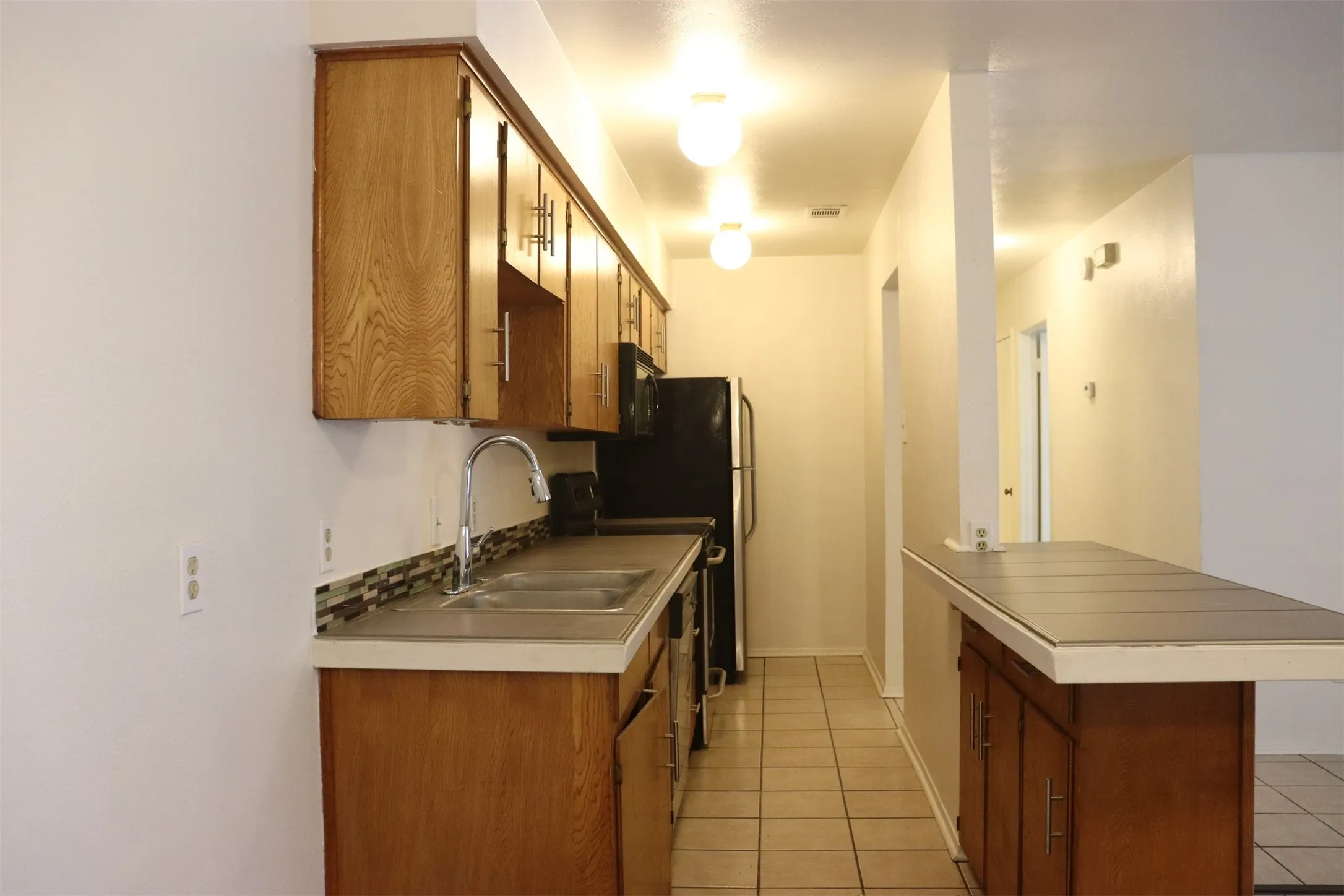 Galley kitchen featuring wood-finish cabinetry, tile flooring, and a double-basin stainless steel sink with a gooseneck faucet
