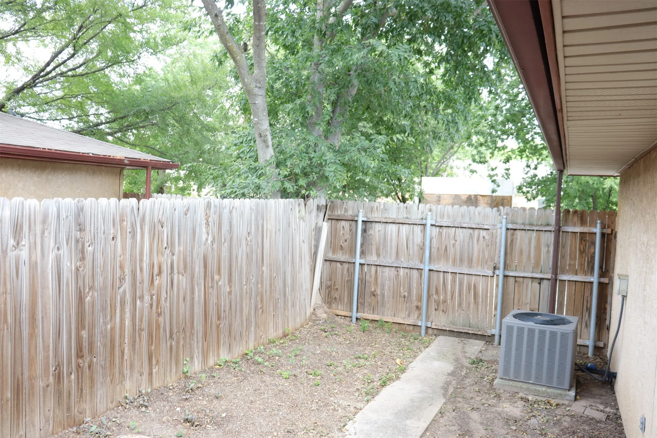 Private outdoor space featuring a wood picket fence, concrete pathway, and covered patio area