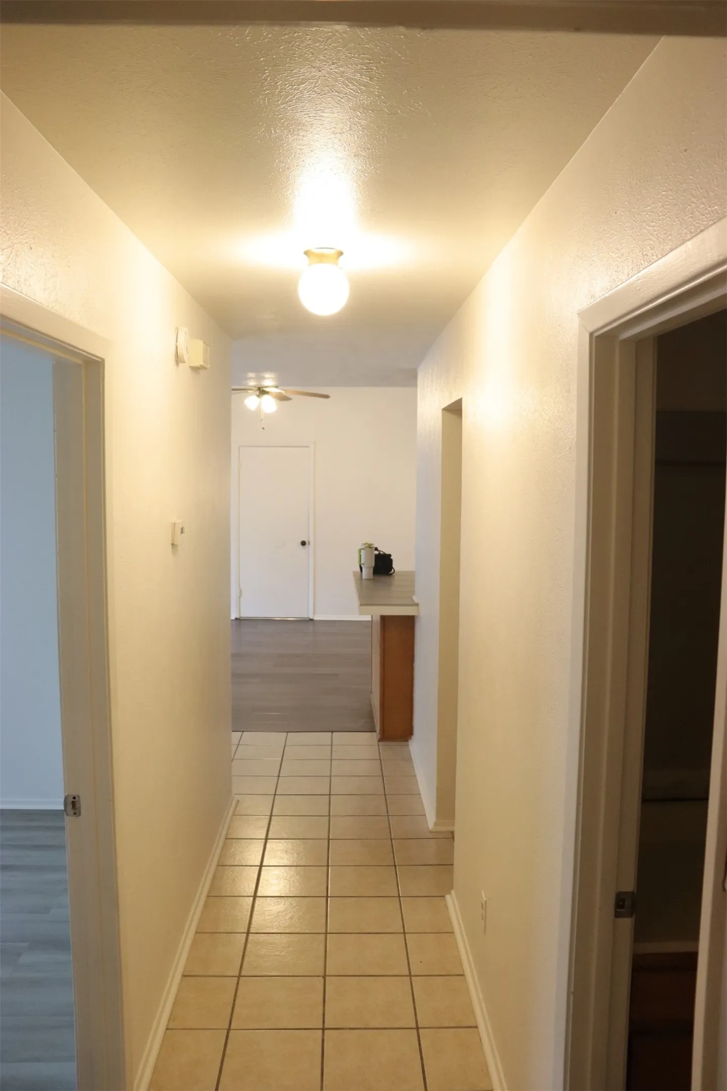 Hallway featuring tile flooring, neutral wall tones, and recessed lighting leading to an open living area with wood-finish flooring and a ceiling fan