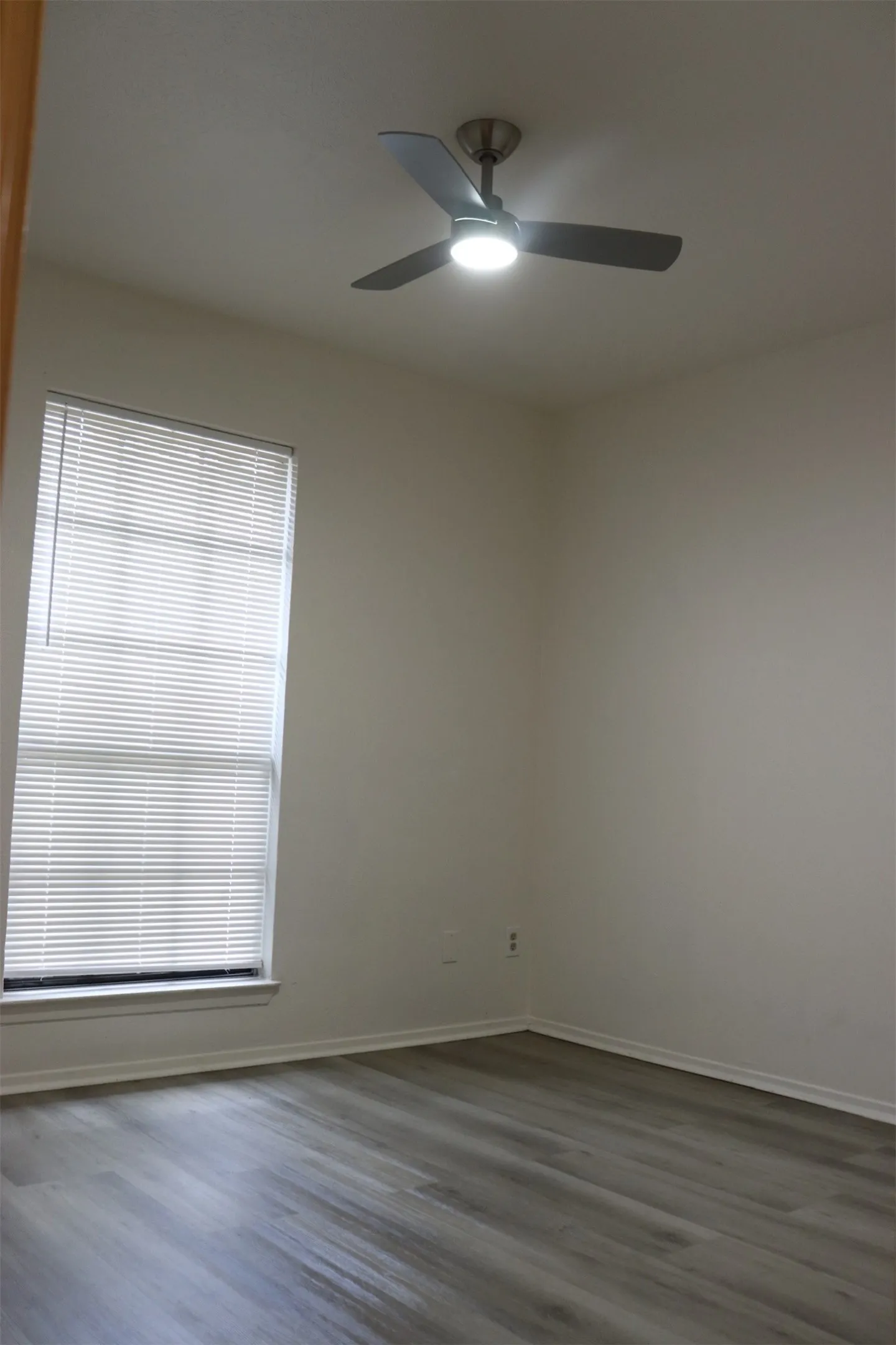 Interior room featuring light gray wood-finish flooring, a window with horizontal blinds, and a ceiling fan with integrated lighting
