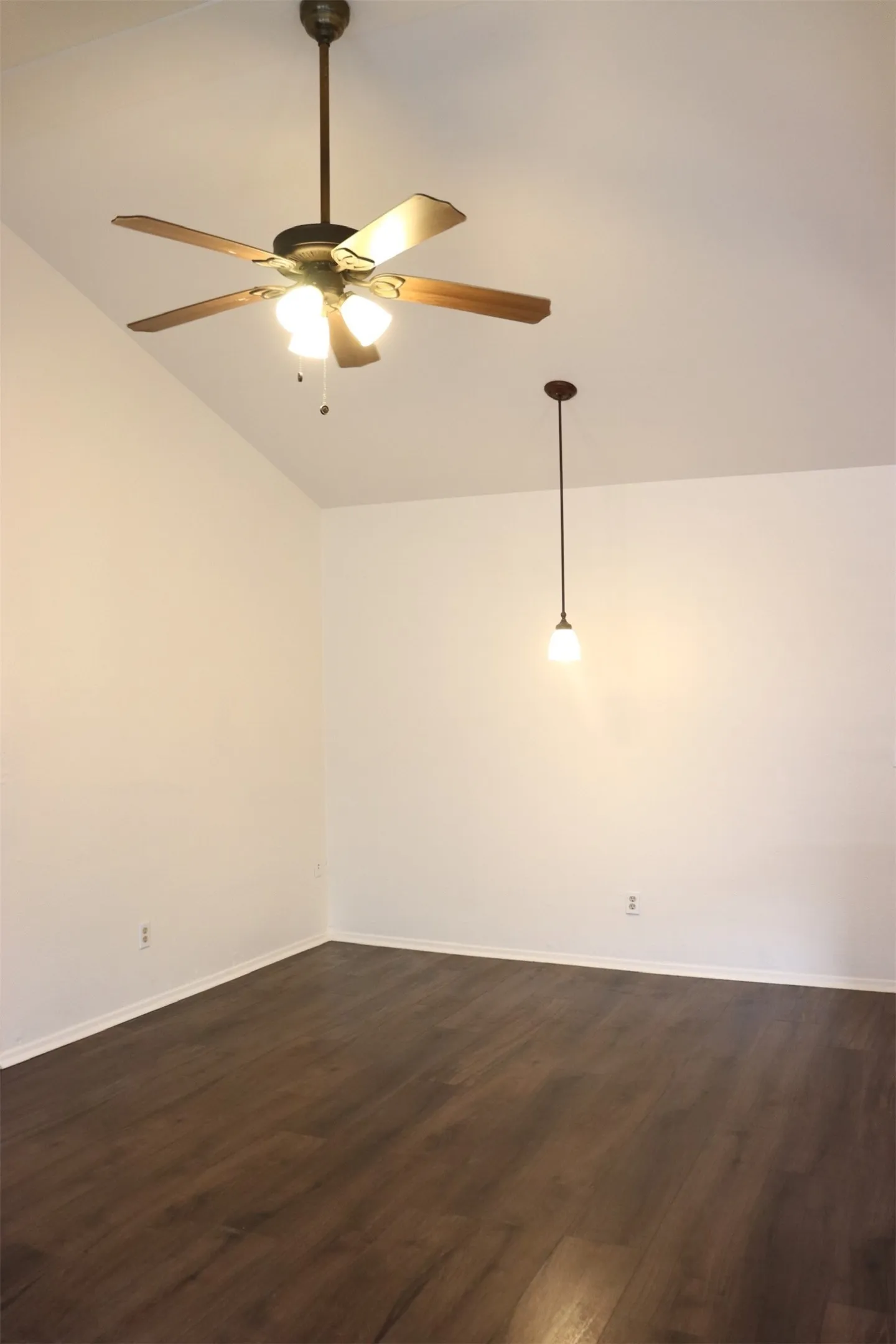 Vaulted ceiling with a ceiling fan and integrated lighting, wood-finish flooring, and a pendant light fixture