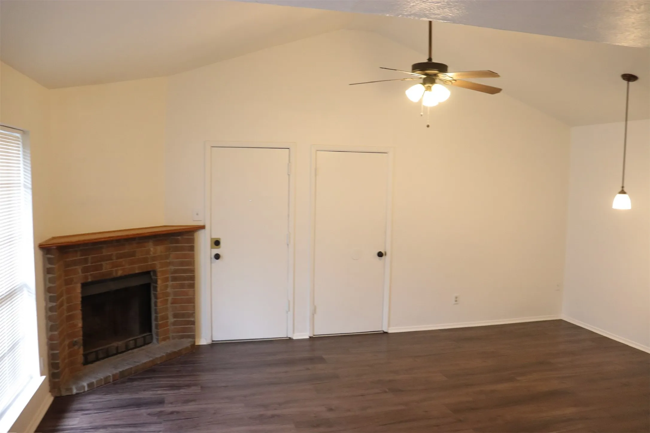 Living area featuring a brick fireplace with a wood mantel, wood-finish flooring, and a vaulted ceiling