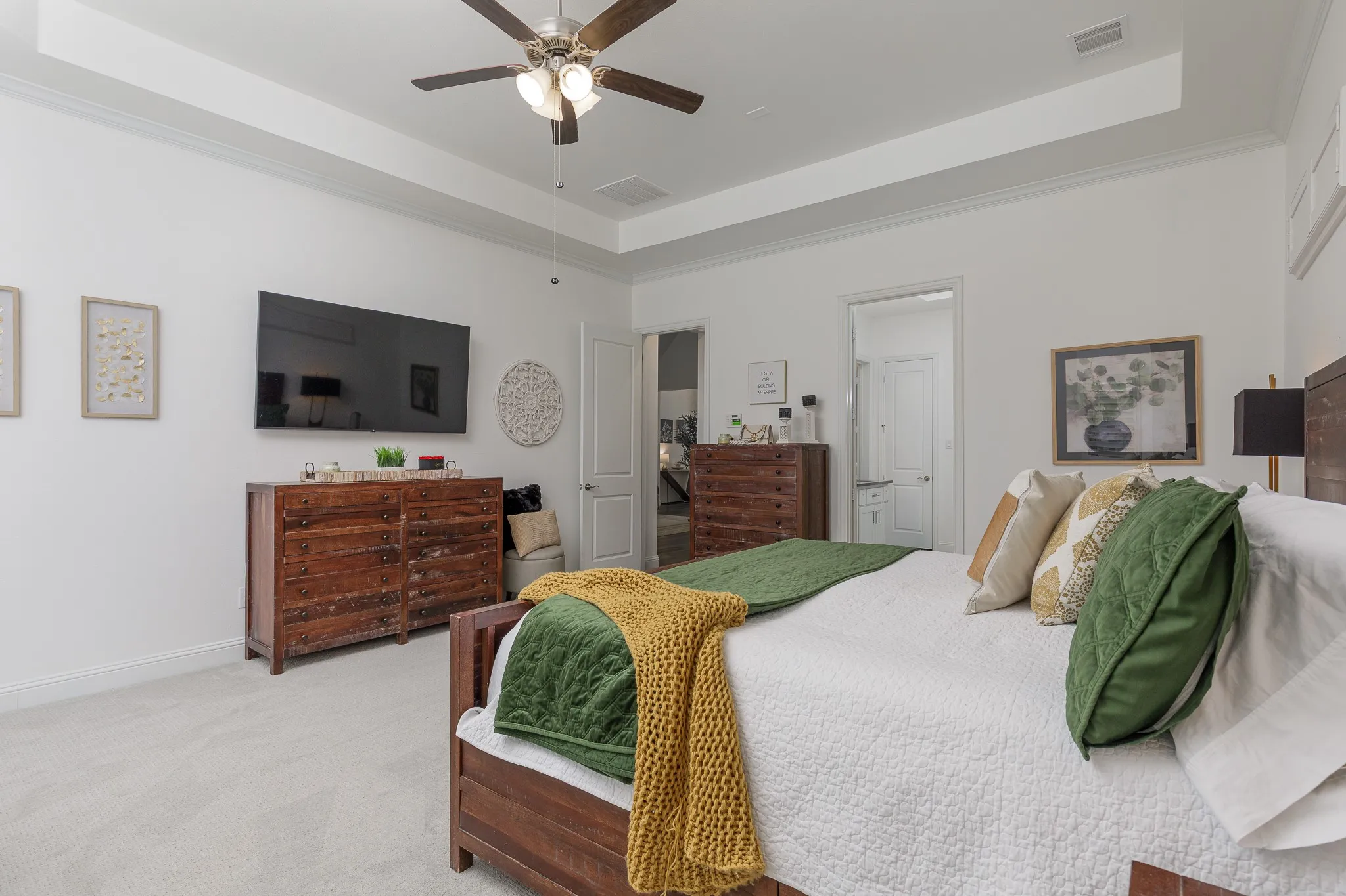 Spacious bedroom featuring light-colored carpeting, a tray ceiling with a ceiling fan, and white walls