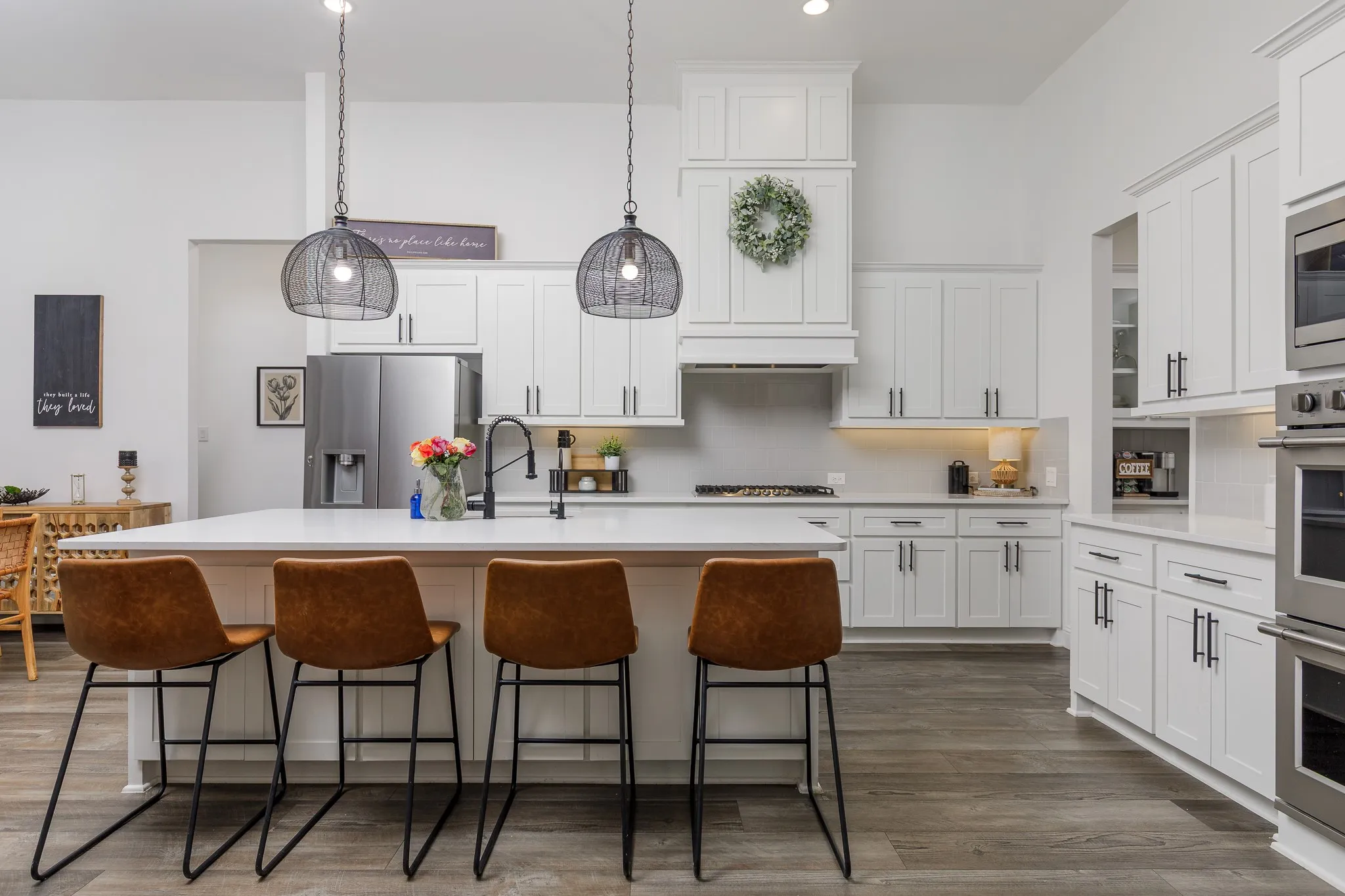 Bright kitchen featuring a substantial island with seating, white shaker cabinetry, stainless steel appliances, and wood-finish flooring