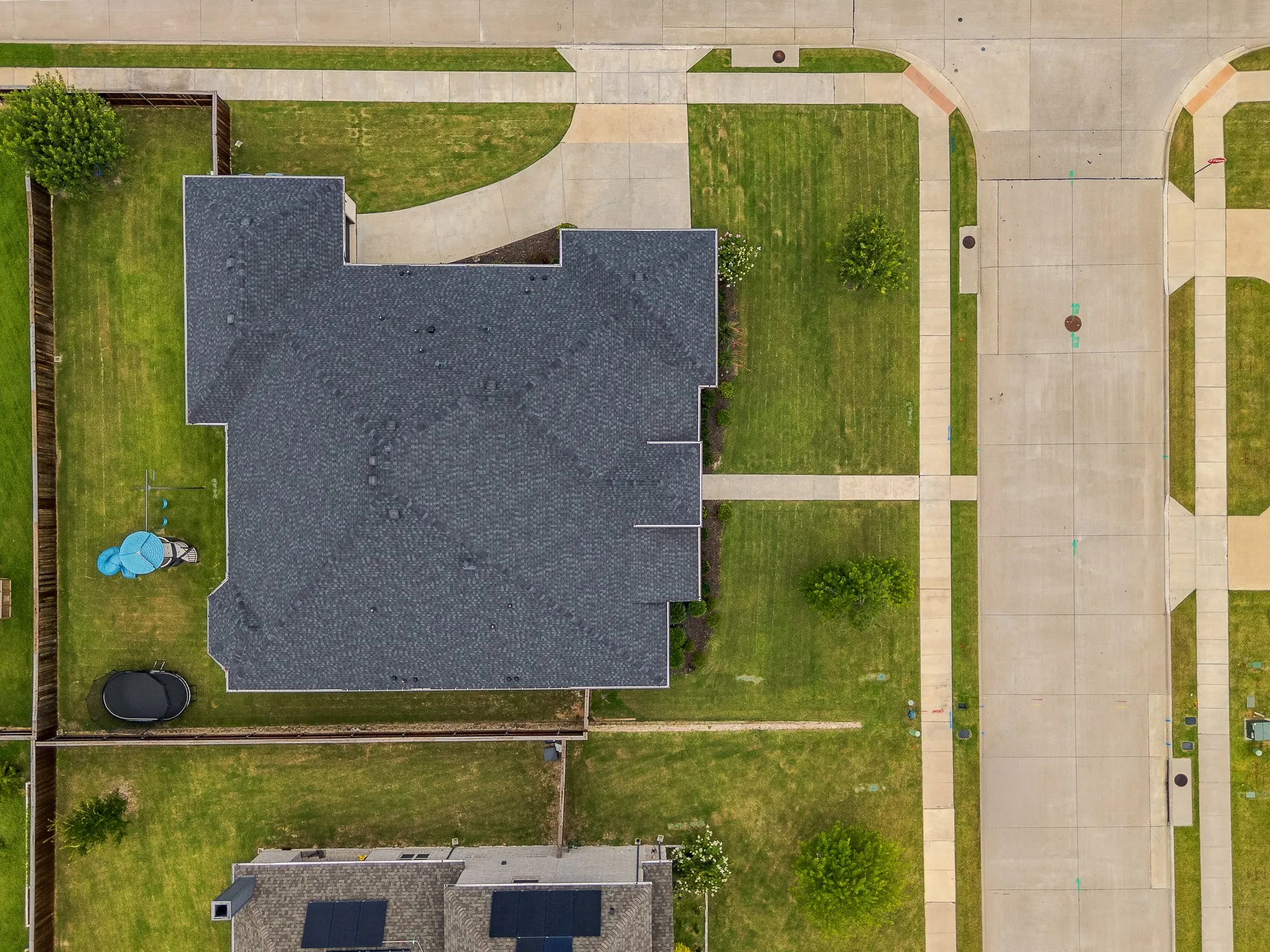 Aerial perspective showcasing a property with a dark shingle roof, a spacious green lawn, and a concrete driveway