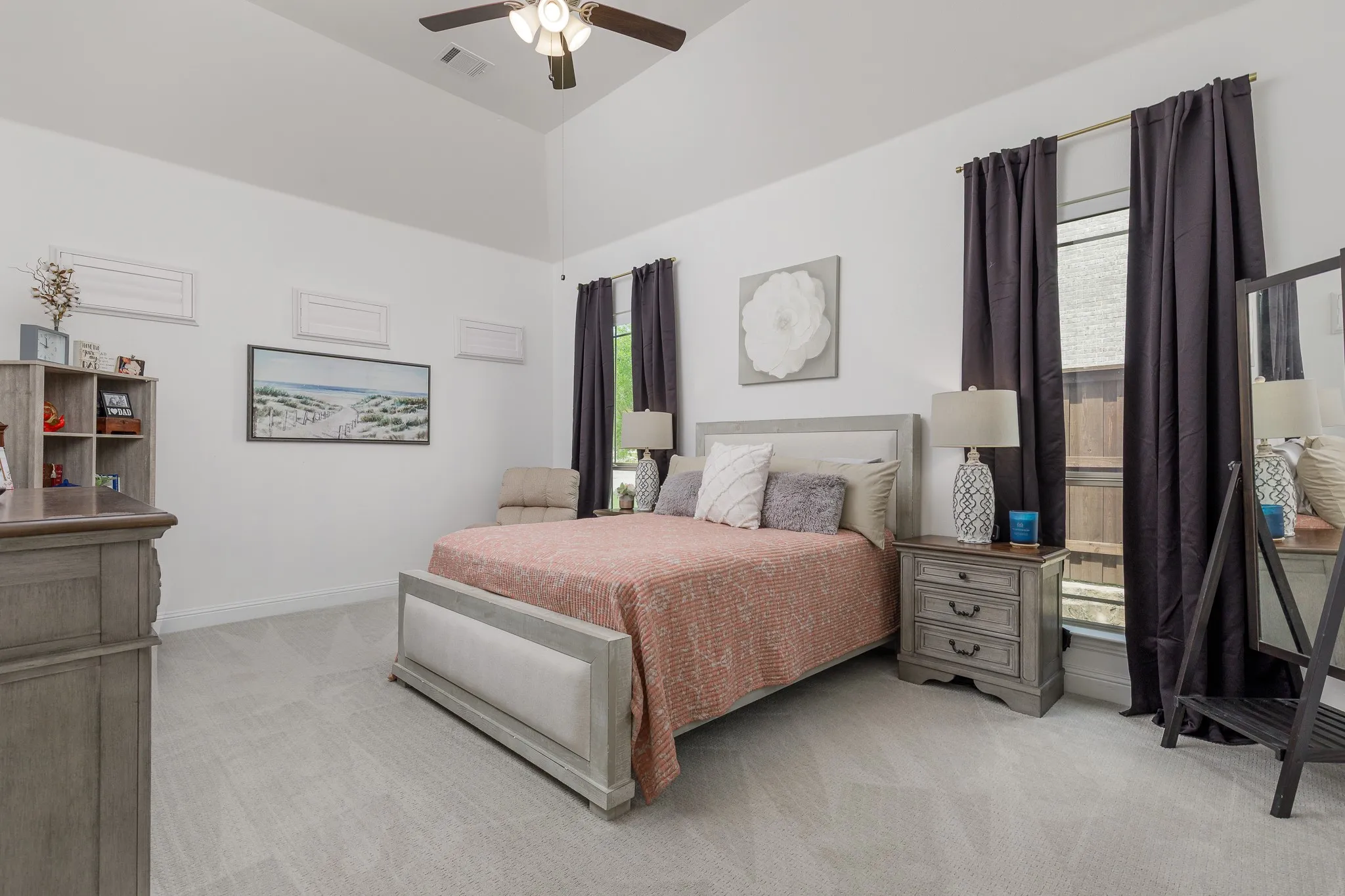Vaulted ceiling with a ceiling fan, light gray carpet flooring, and two large windows with dark curtains