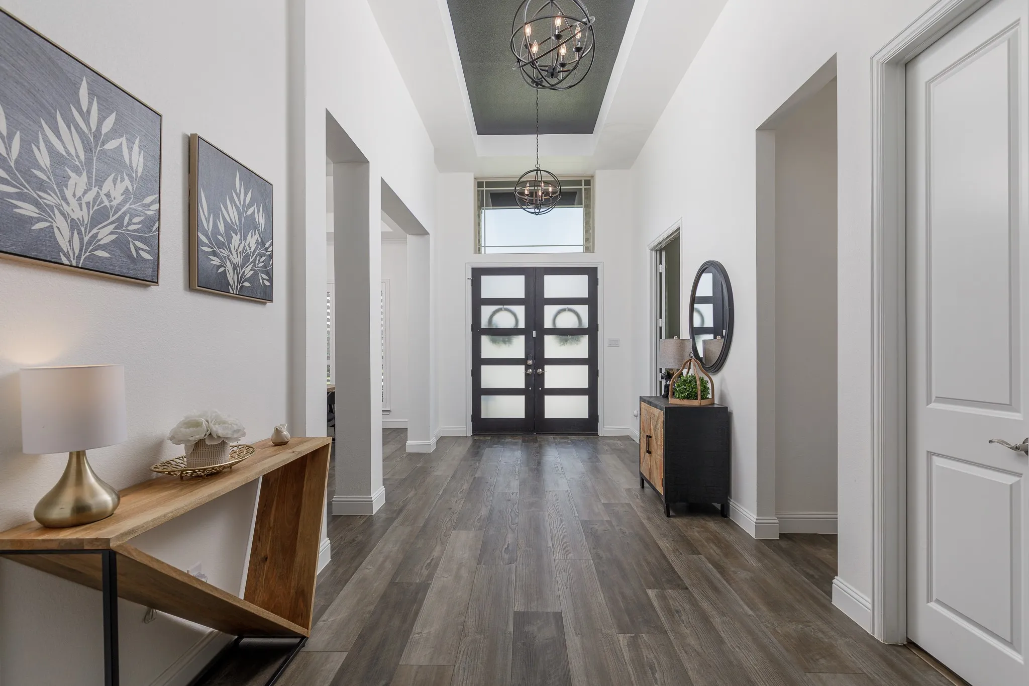 Spacious entryway featuring wood-finish flooring, a double-door entry with frosted glass panels, transom windows, and a tray ceiling with recessed lighting