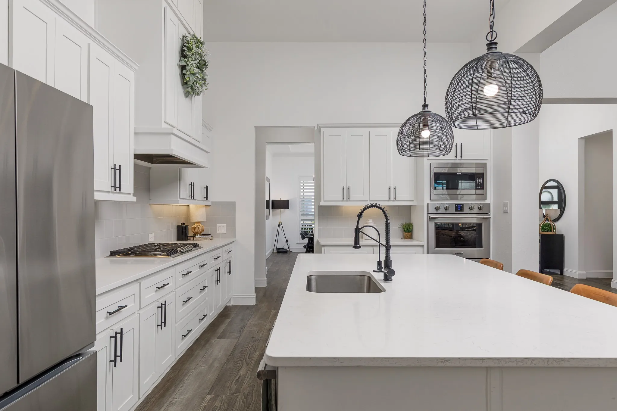 Modern kitchen featuring an expansive island with an undermount sink and matte black faucet, white cabinetry with dark hardware, stainless steel appliances, and wood-finish flooring