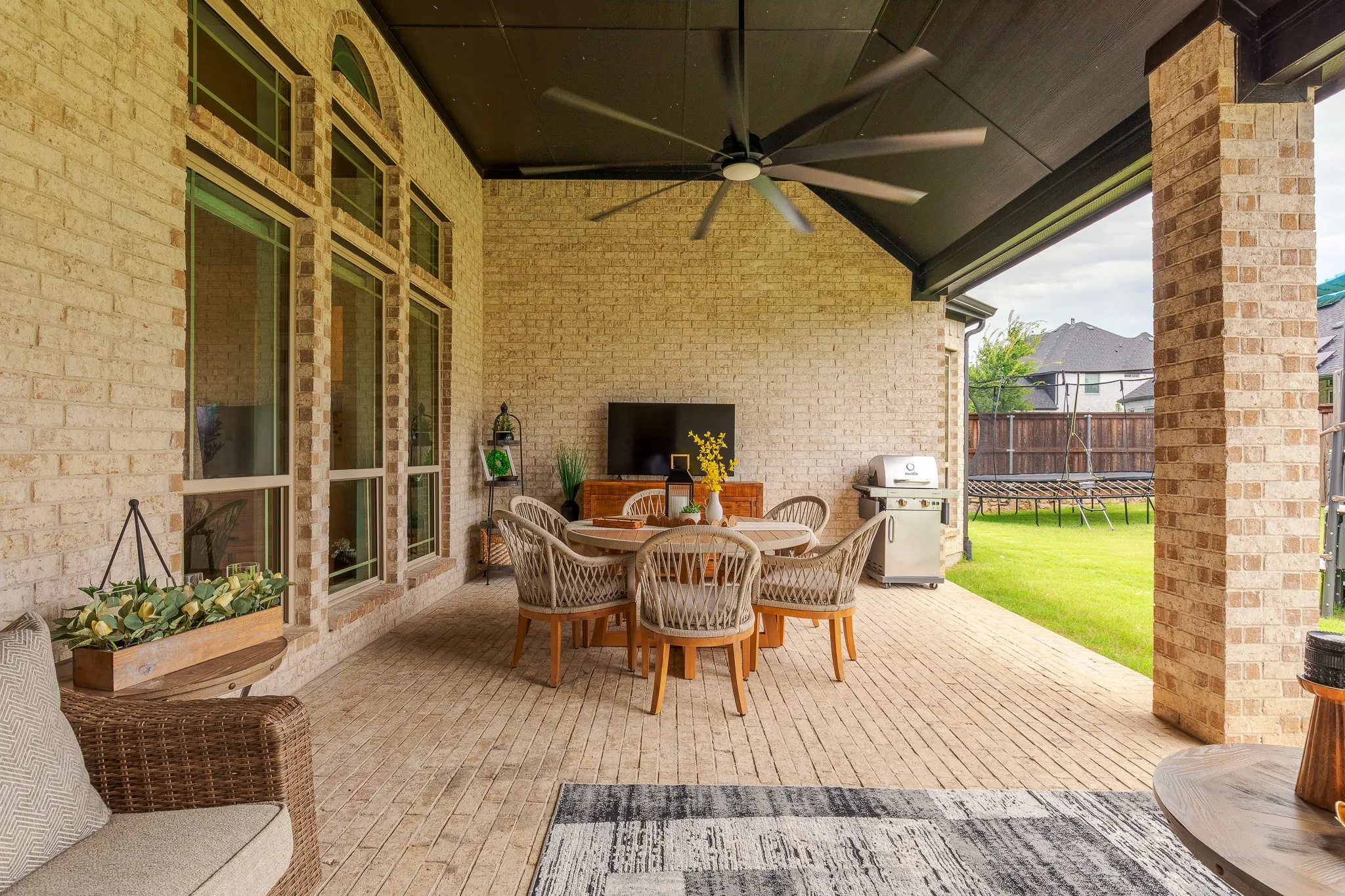 Covered outdoor patio featuring light-toned brick construction and a ceiling fan