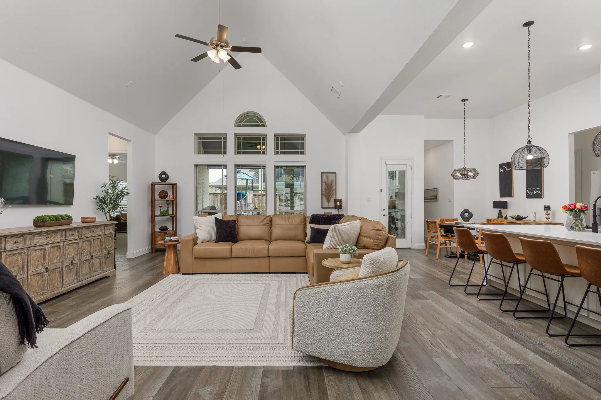 Vaulted ceiling living area featuring wood-finish flooring, a contemporary ceiling fan, and large windows with an arched transom