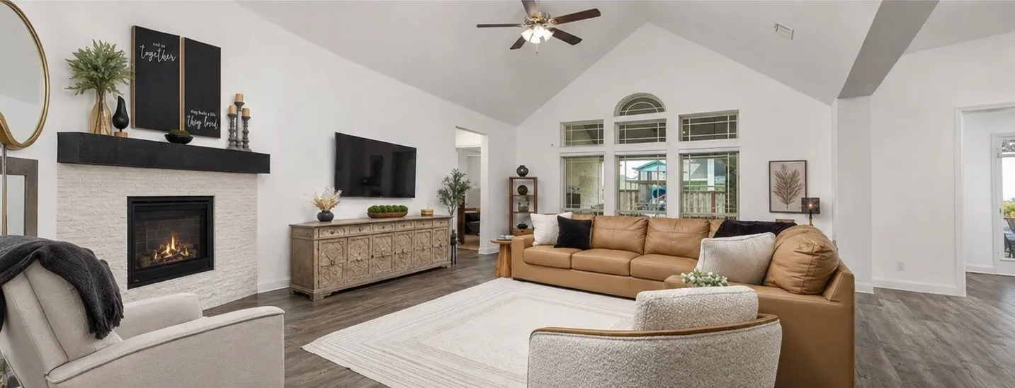 Vaulted ceiling, stone-surround fireplace with a dark wood mantel, large arched windows, wood-finish flooring, and a ceiling fan