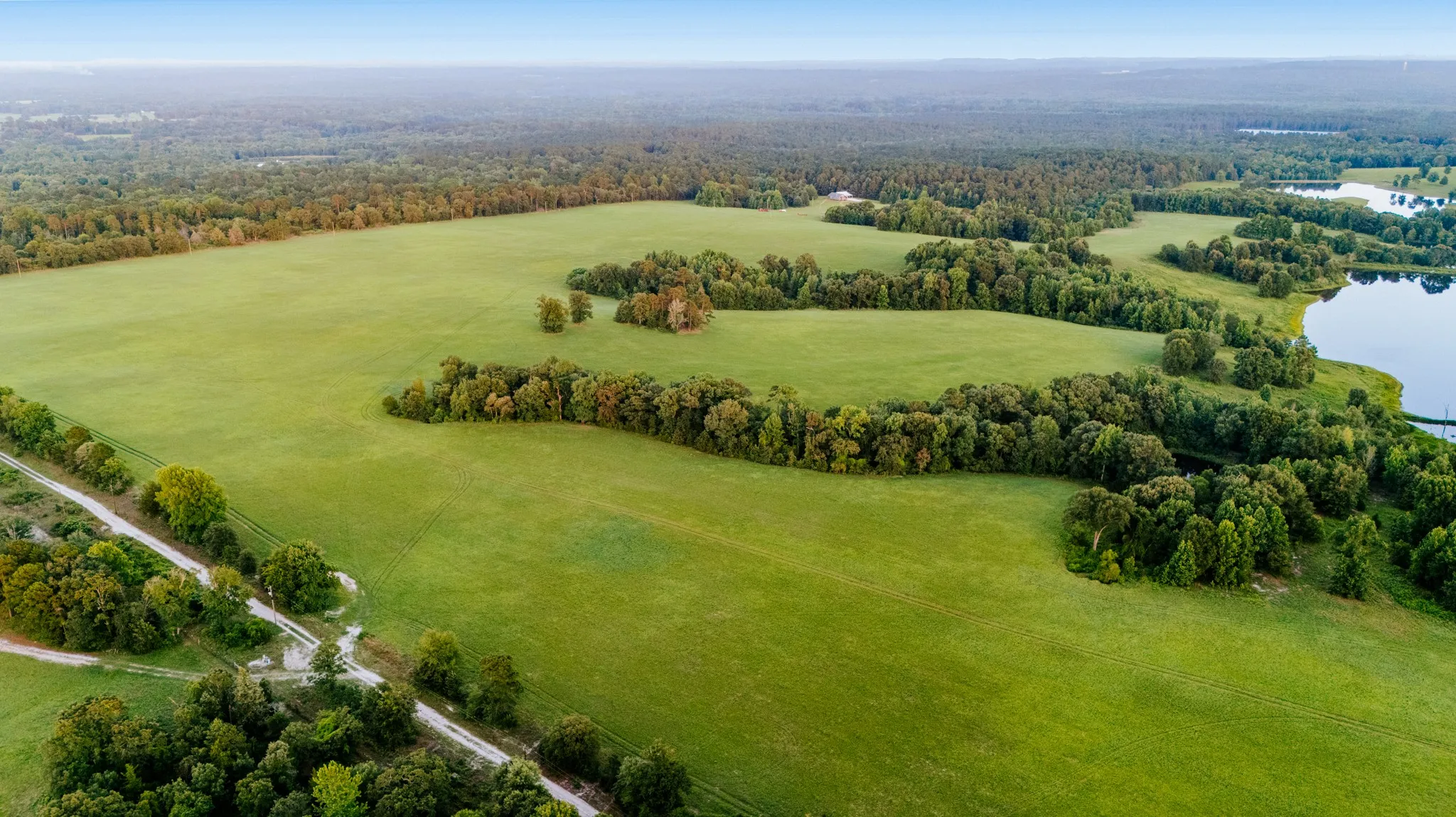 Expansive green acreage featuring natural tree lines and a tranquil body of water