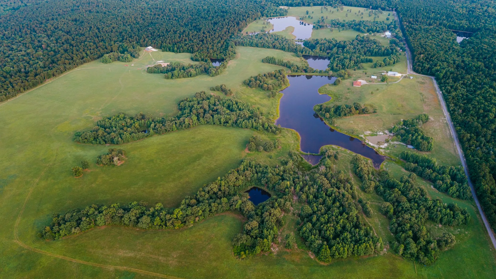 Expansive acreage featuring multiple ponds, open pastures, dense tree lines, and scattered structures
