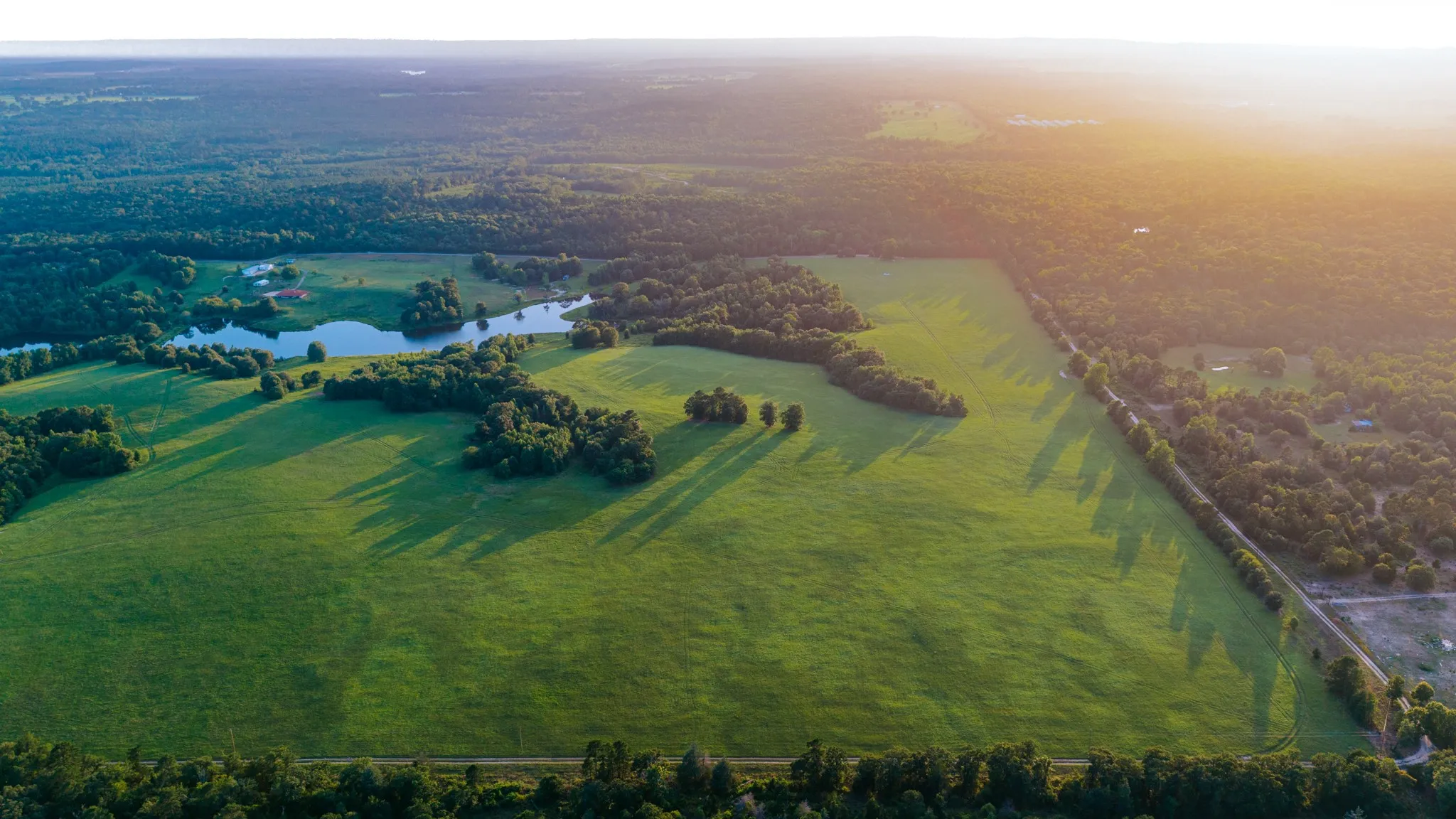 Expansive green fields bordered by mature tree lines and a significant body of water