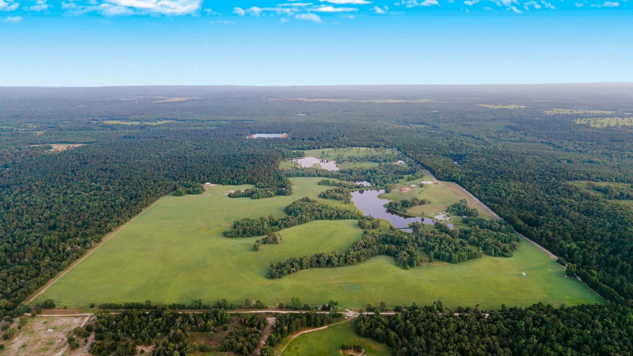 Expansive land parcel featuring open fields, dense woodlands, and multiple bodies of water